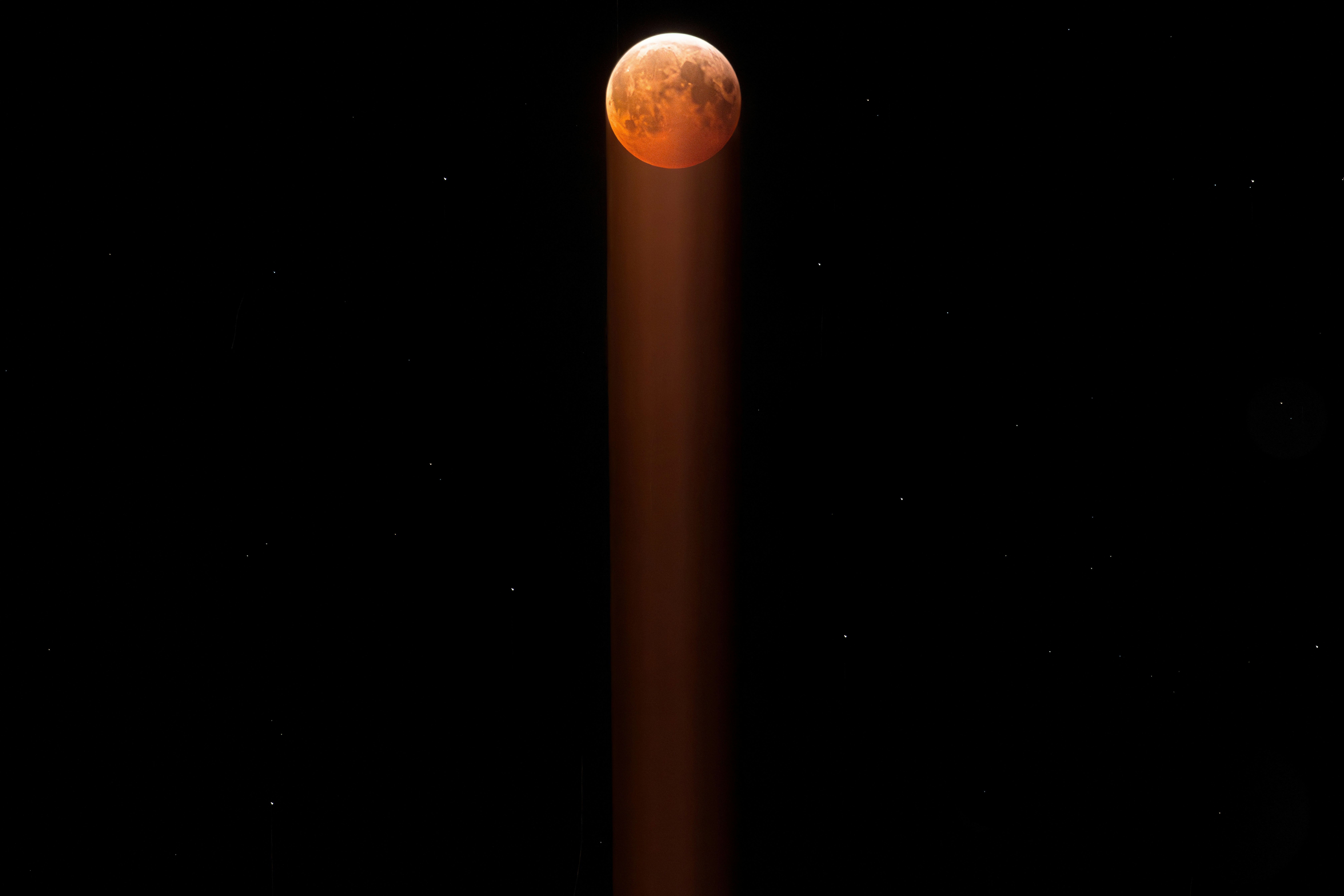 Blood moon in starry night sky with light beam