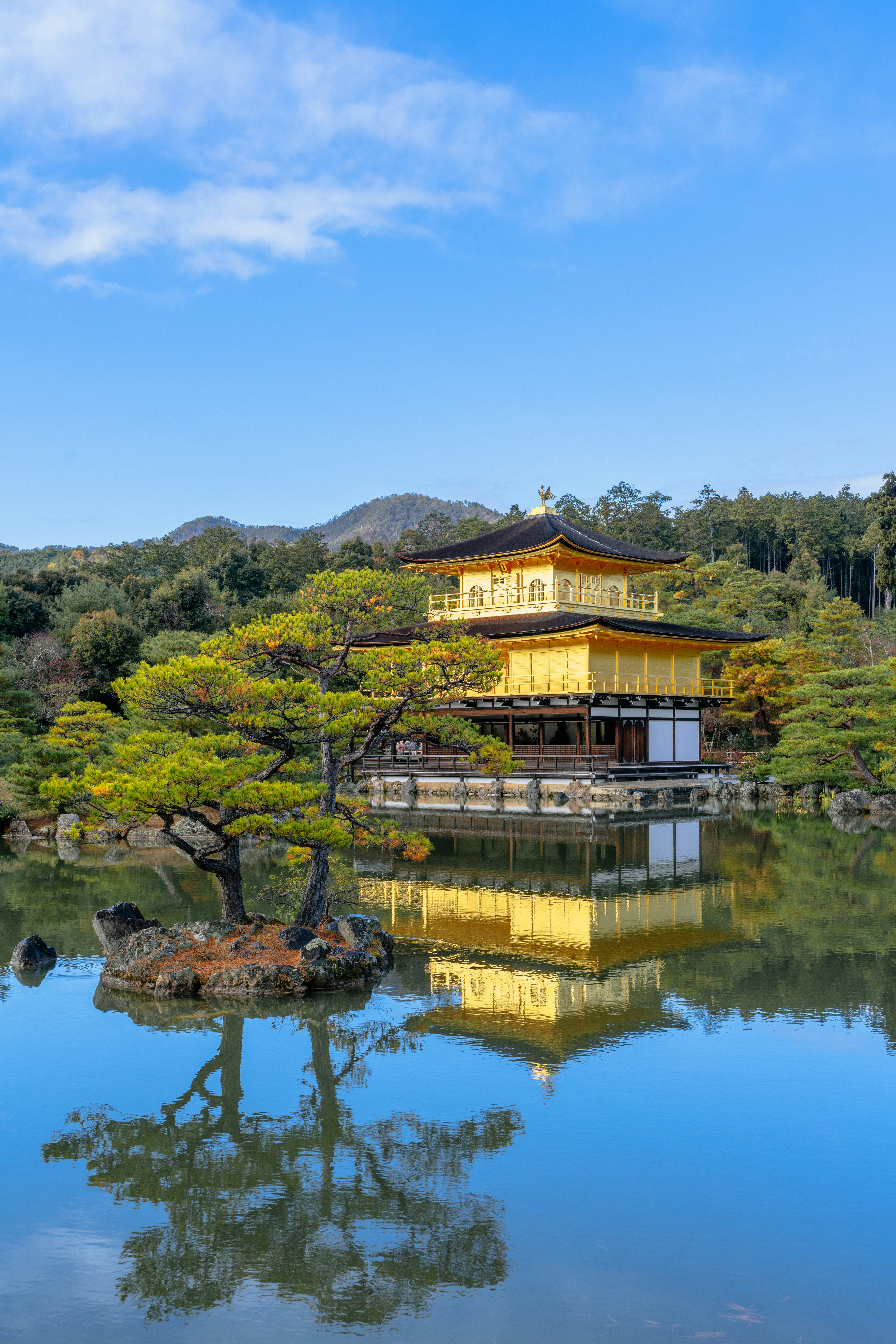 Golden pavilion temple reflected in calm water surrounded by trees.