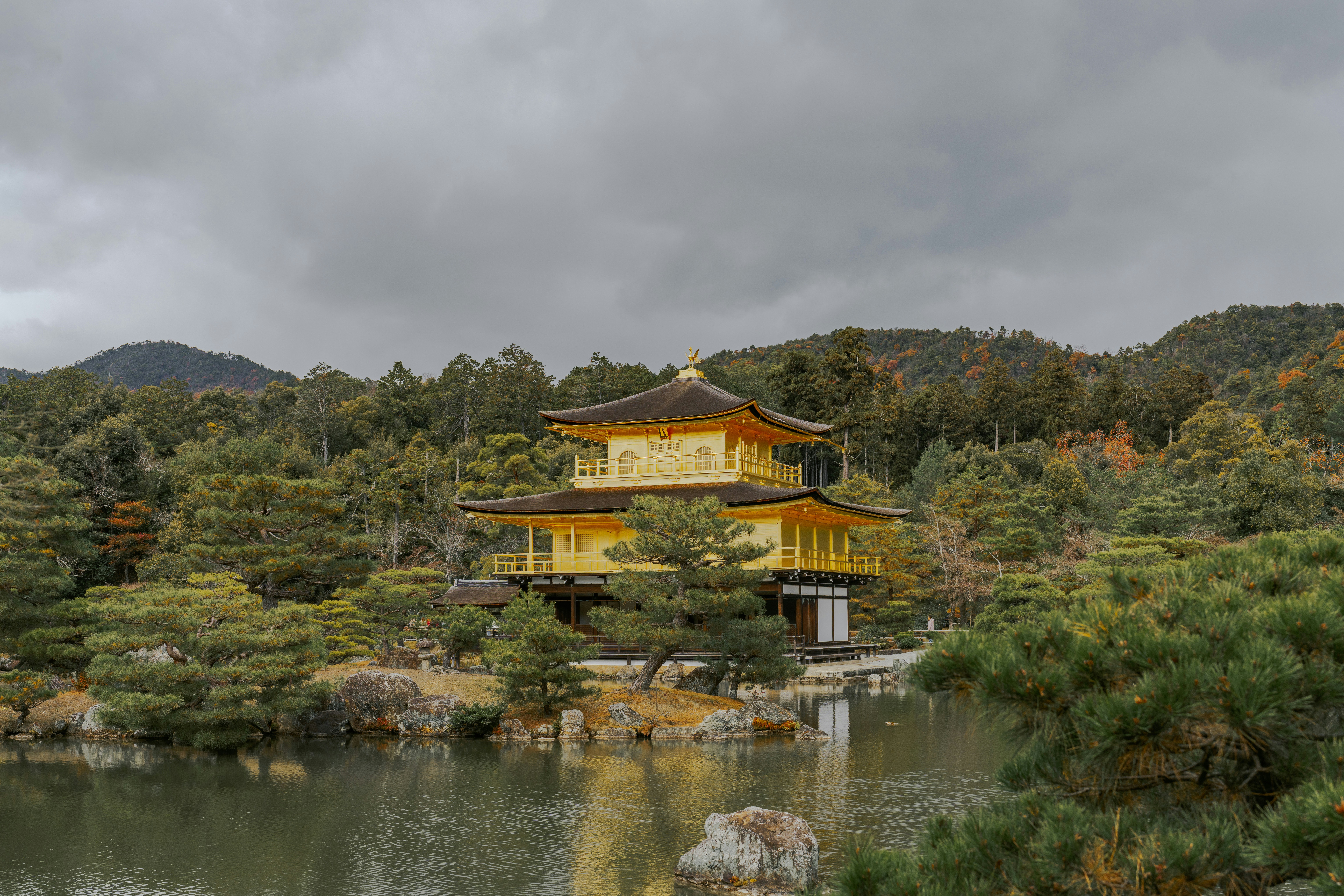 Golden pavilion temple surrounded by autumn trees and water.