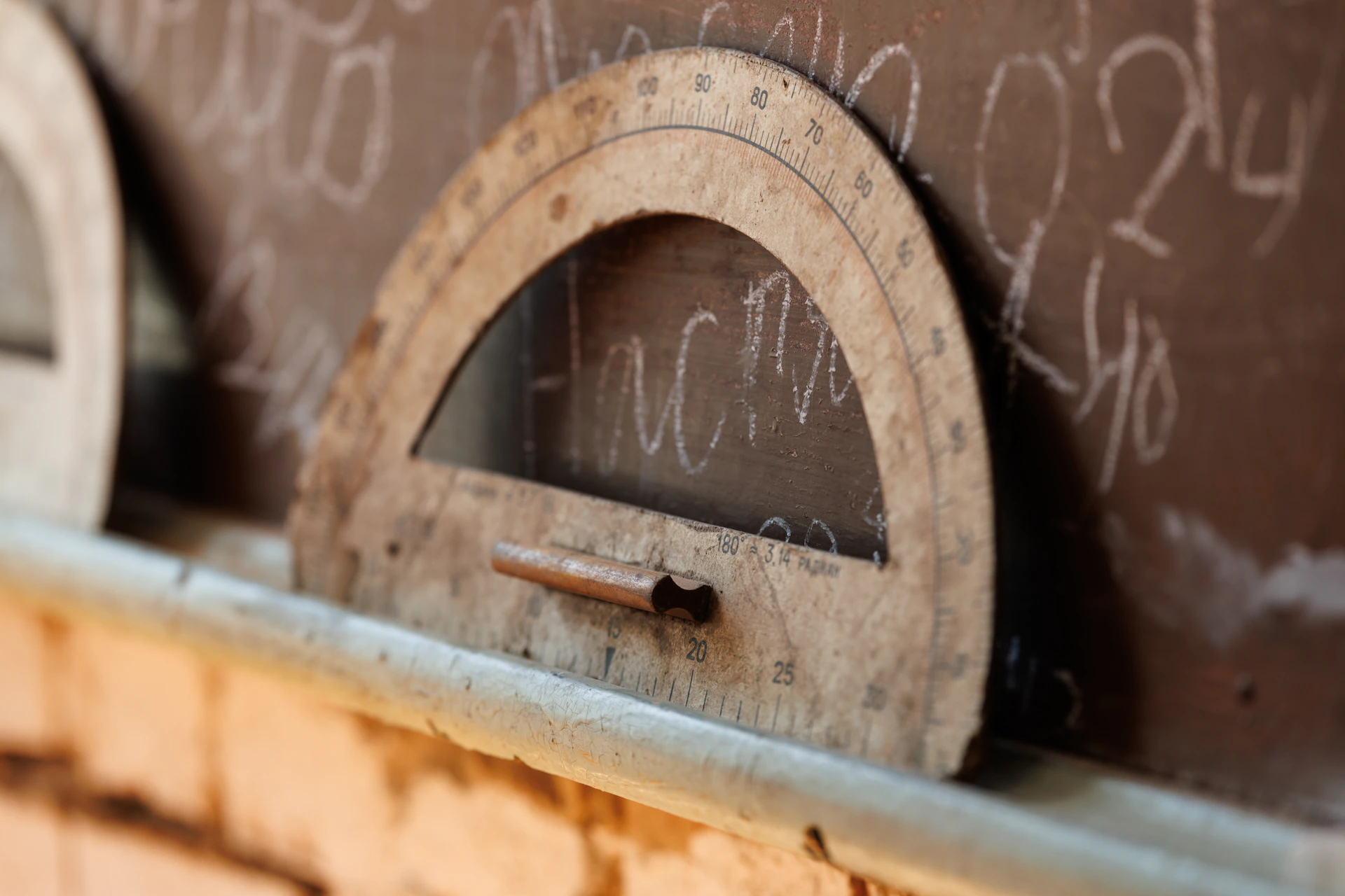 A wooden protractor rests on a chalkboard