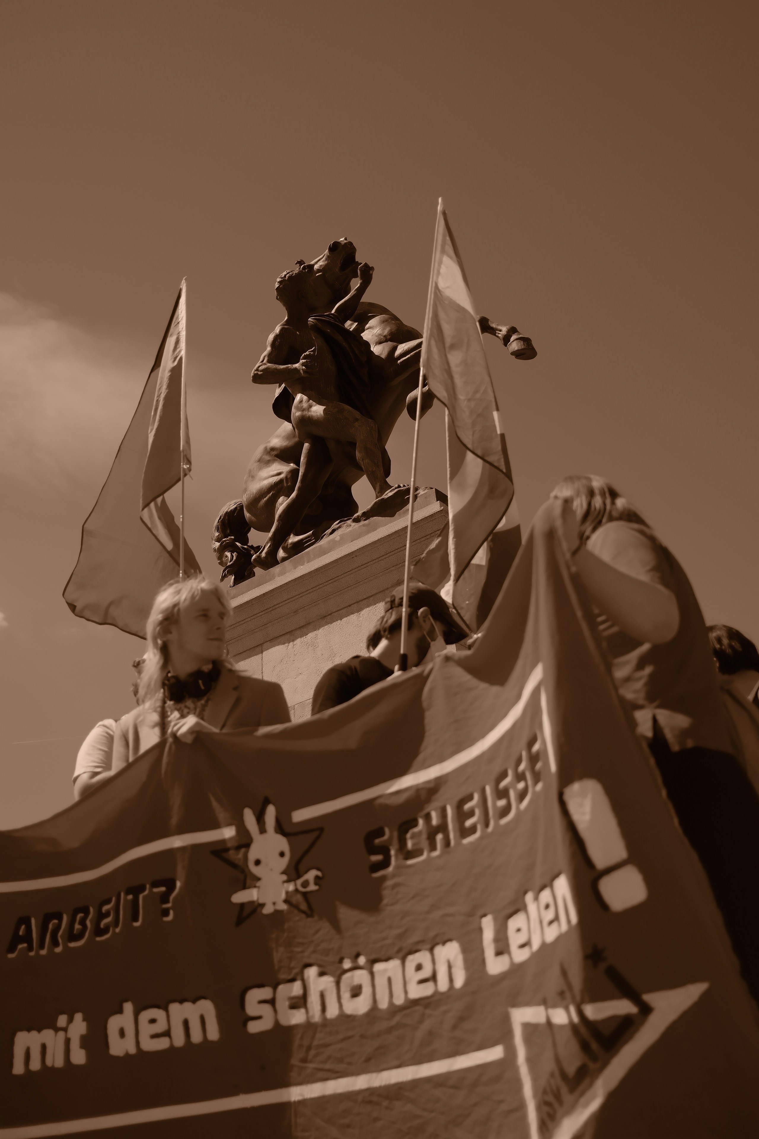 Gente sosteniendo una pancarta con banderas y un monumento.