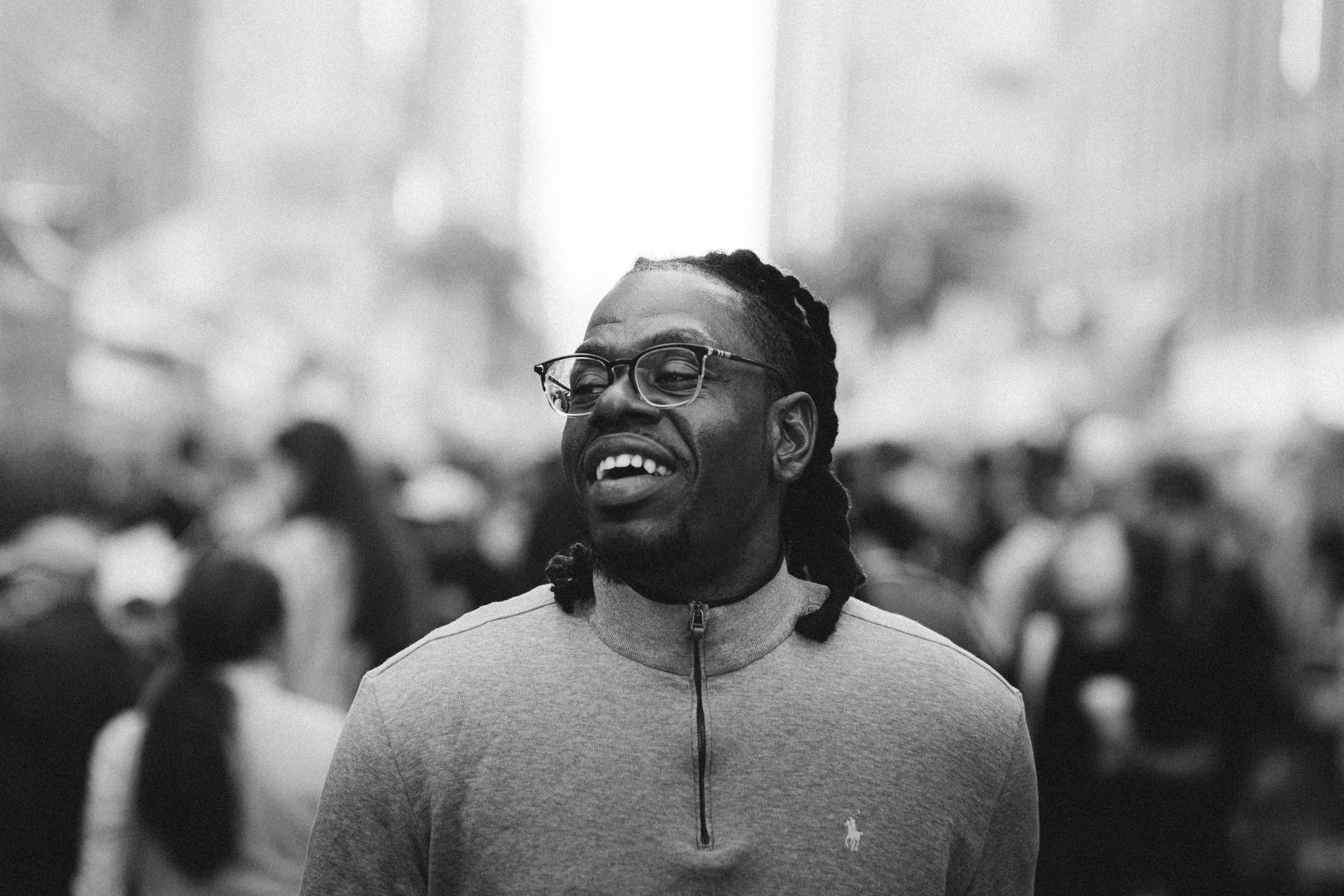 A smiling man with glasses and dreadlocks in a crowd.