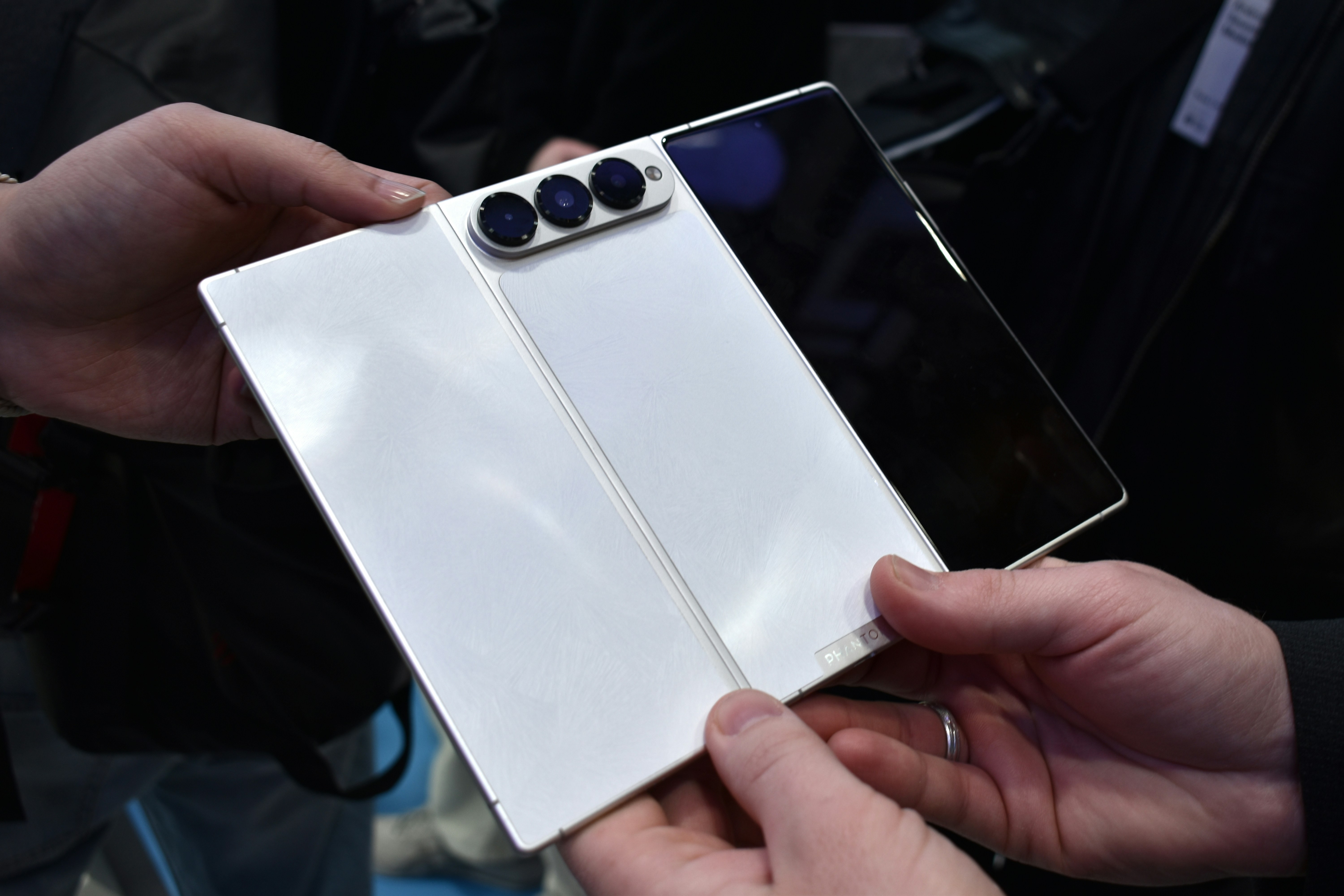 Tangan memegang smartphone lipat putih dengan tiga kamera.
