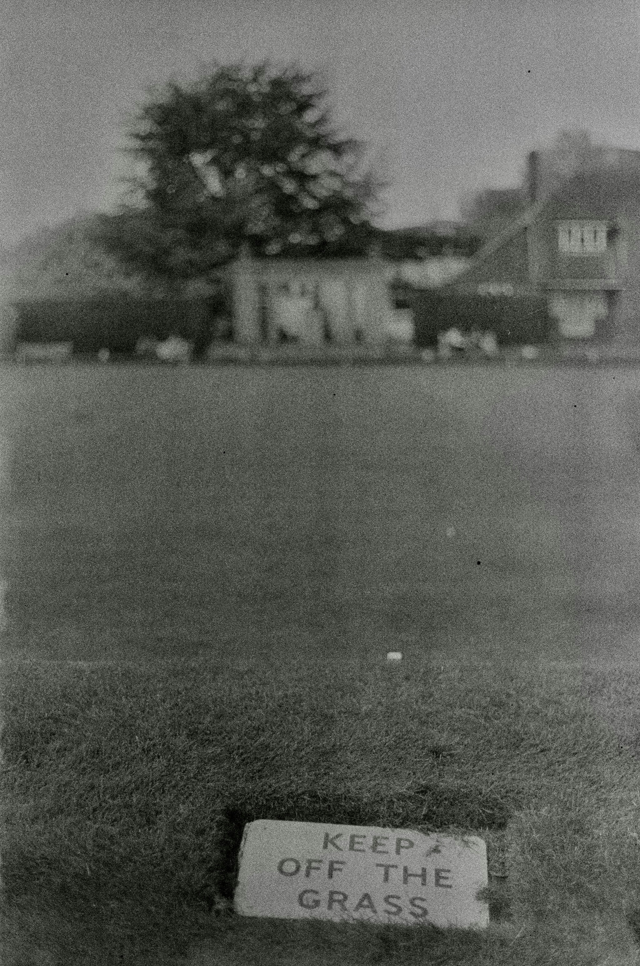 A sign reads "keep off the grass" on a lawn.
