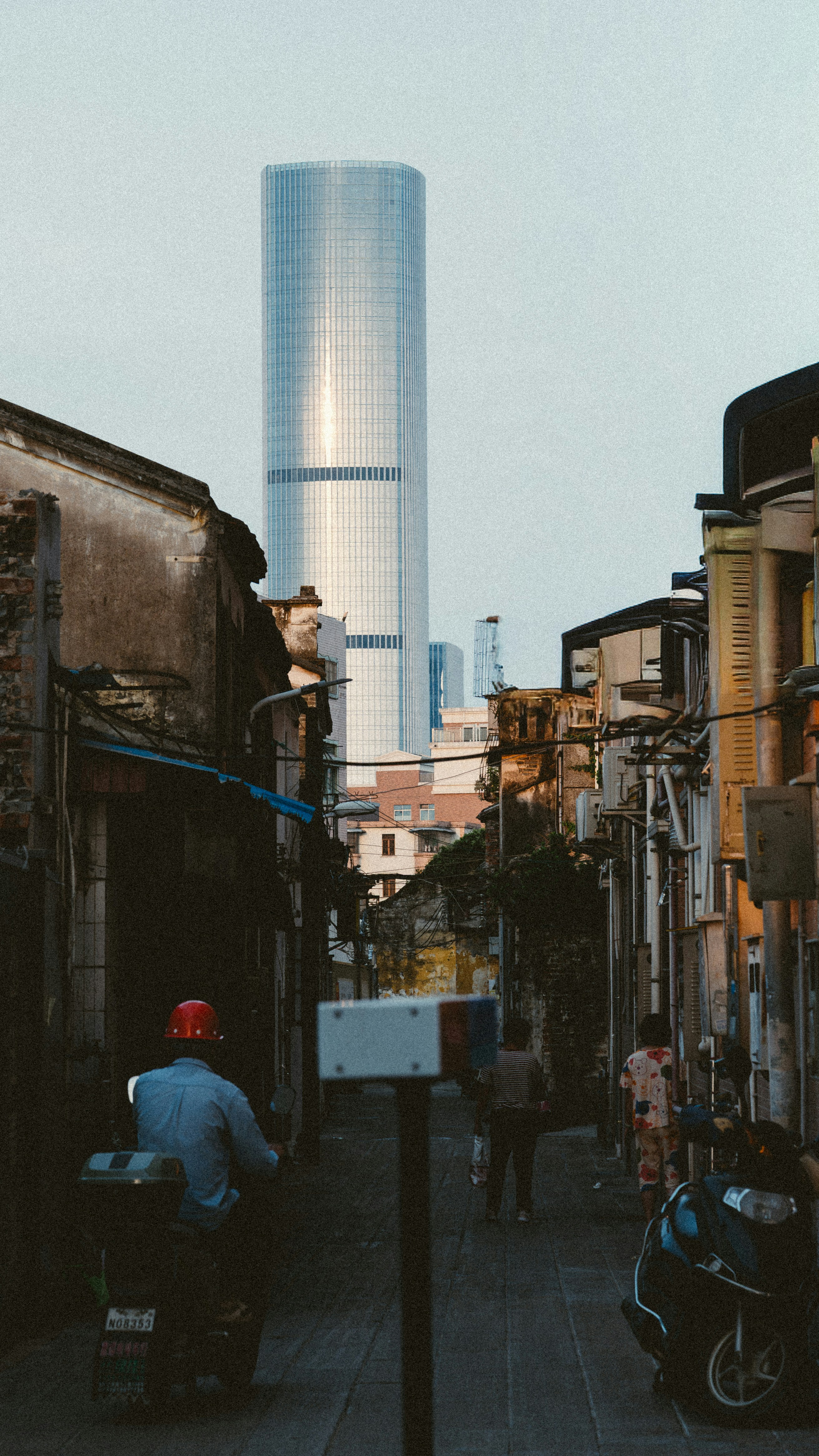 Modern skyscraper looms over old street with people and scooter