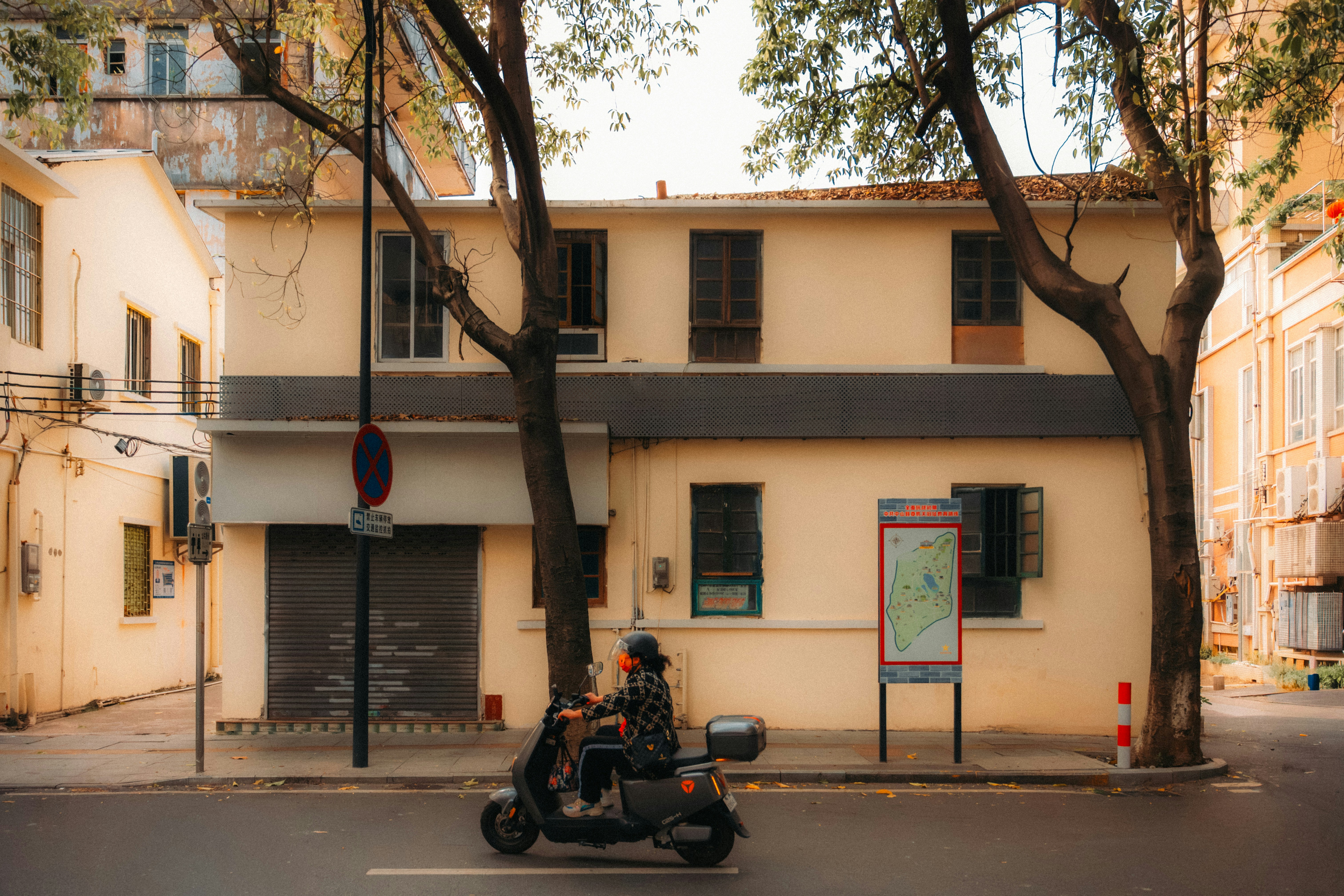 Person rides a scooter past a yellow building.