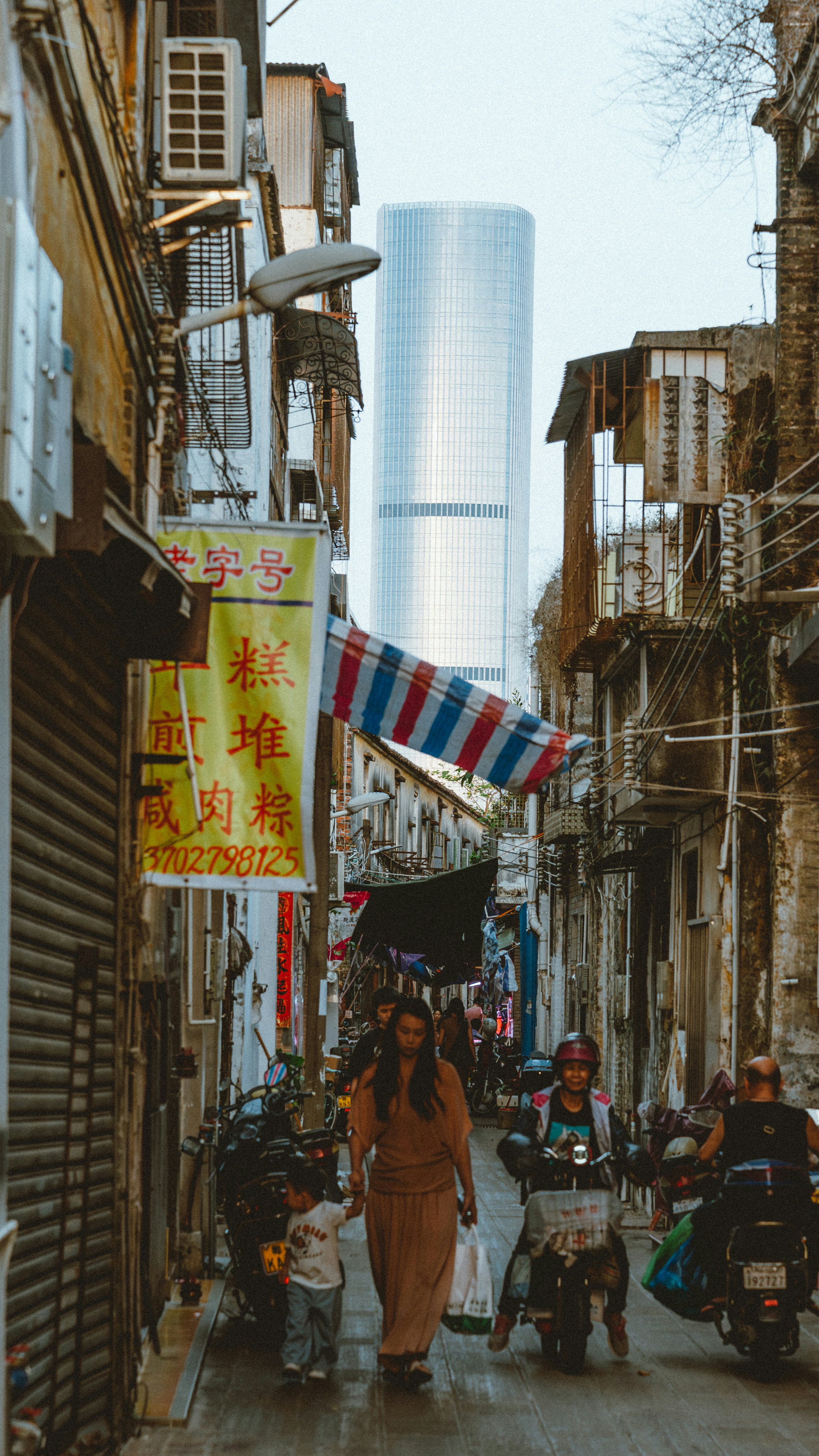 A narrow alleyway with people and a skyscraper in background.
