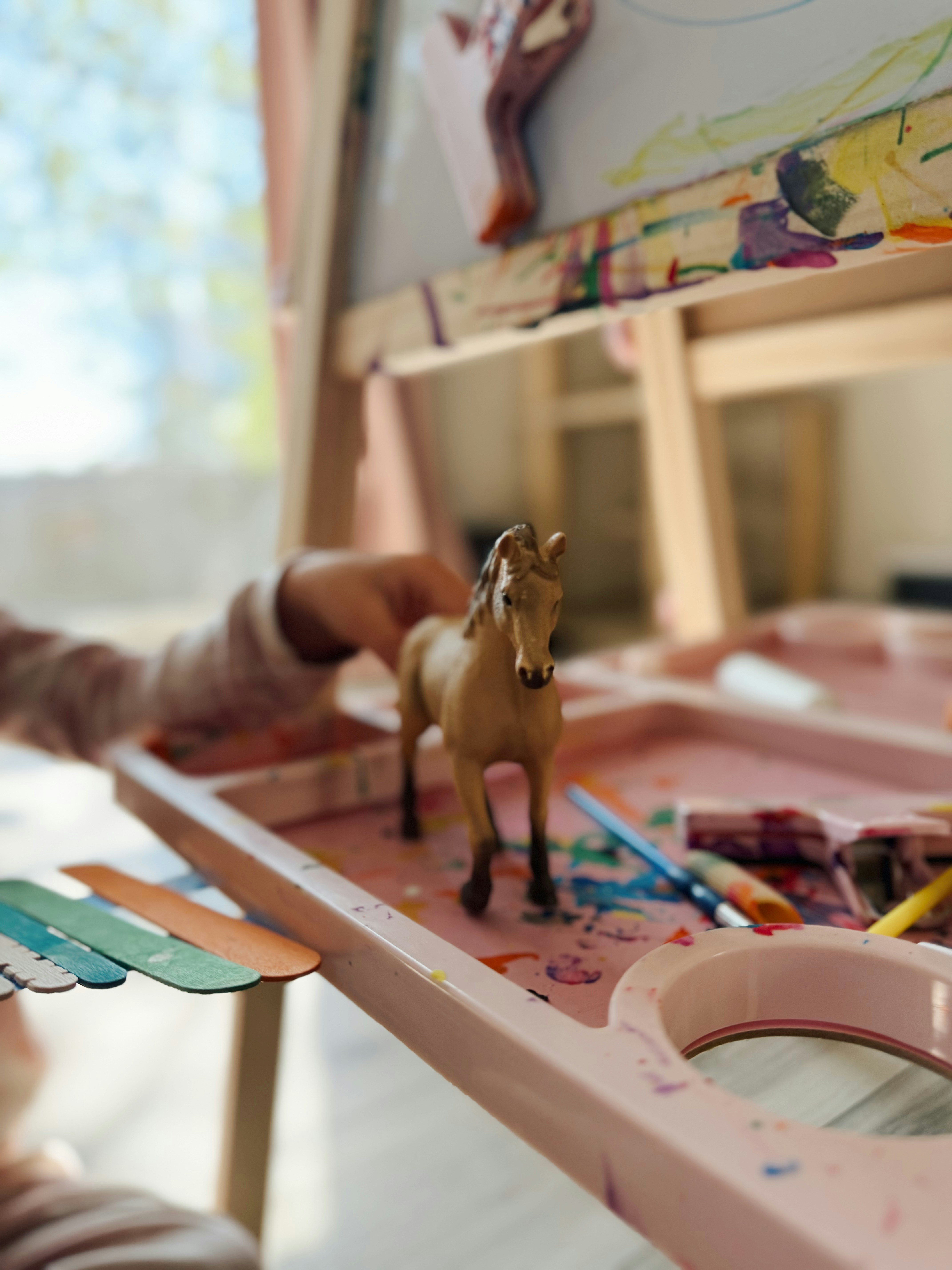 Child's hand reaches for toy horse near art supplies.