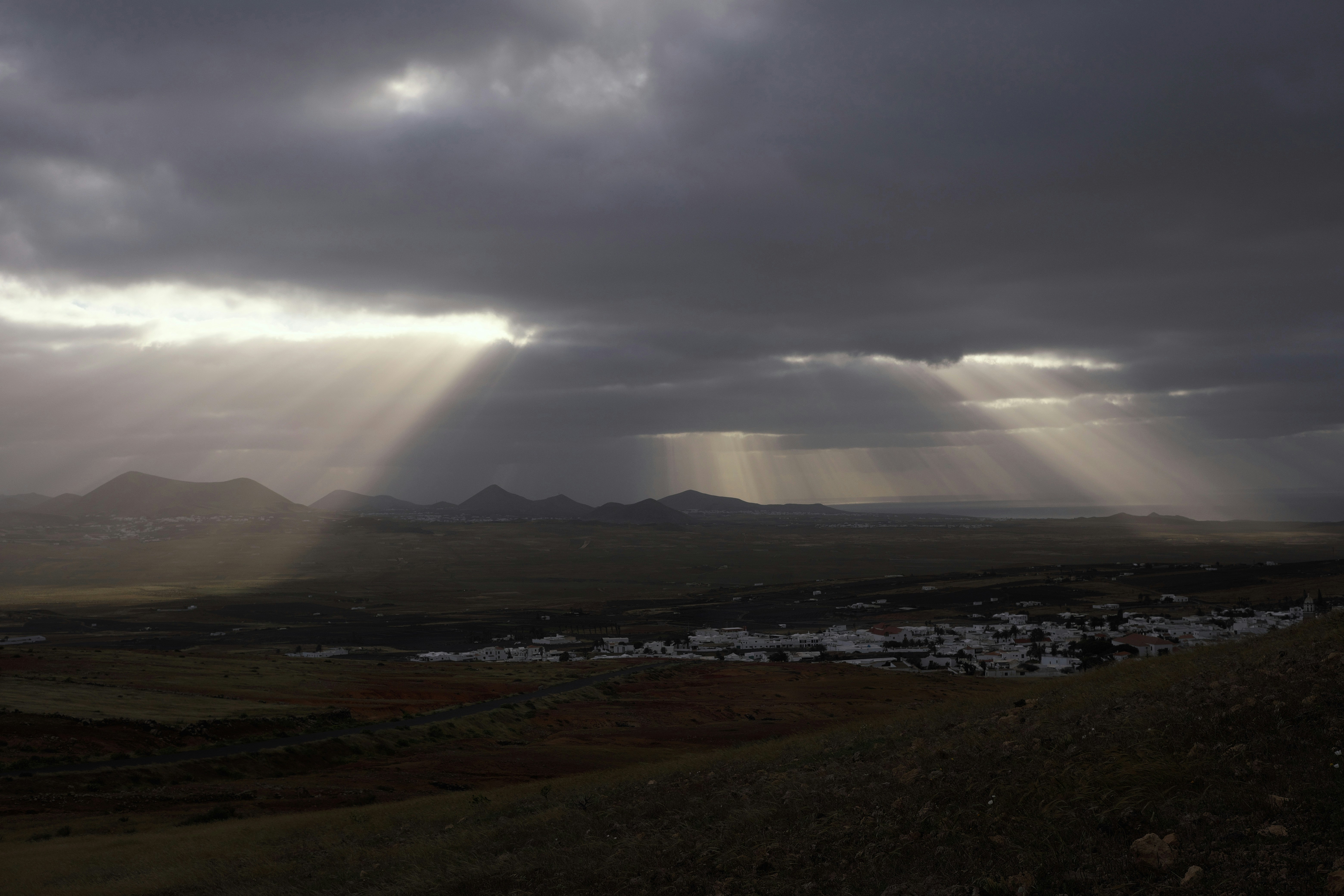 Raios de sol rompendo nuvens escuras sobre uma pequena vila.