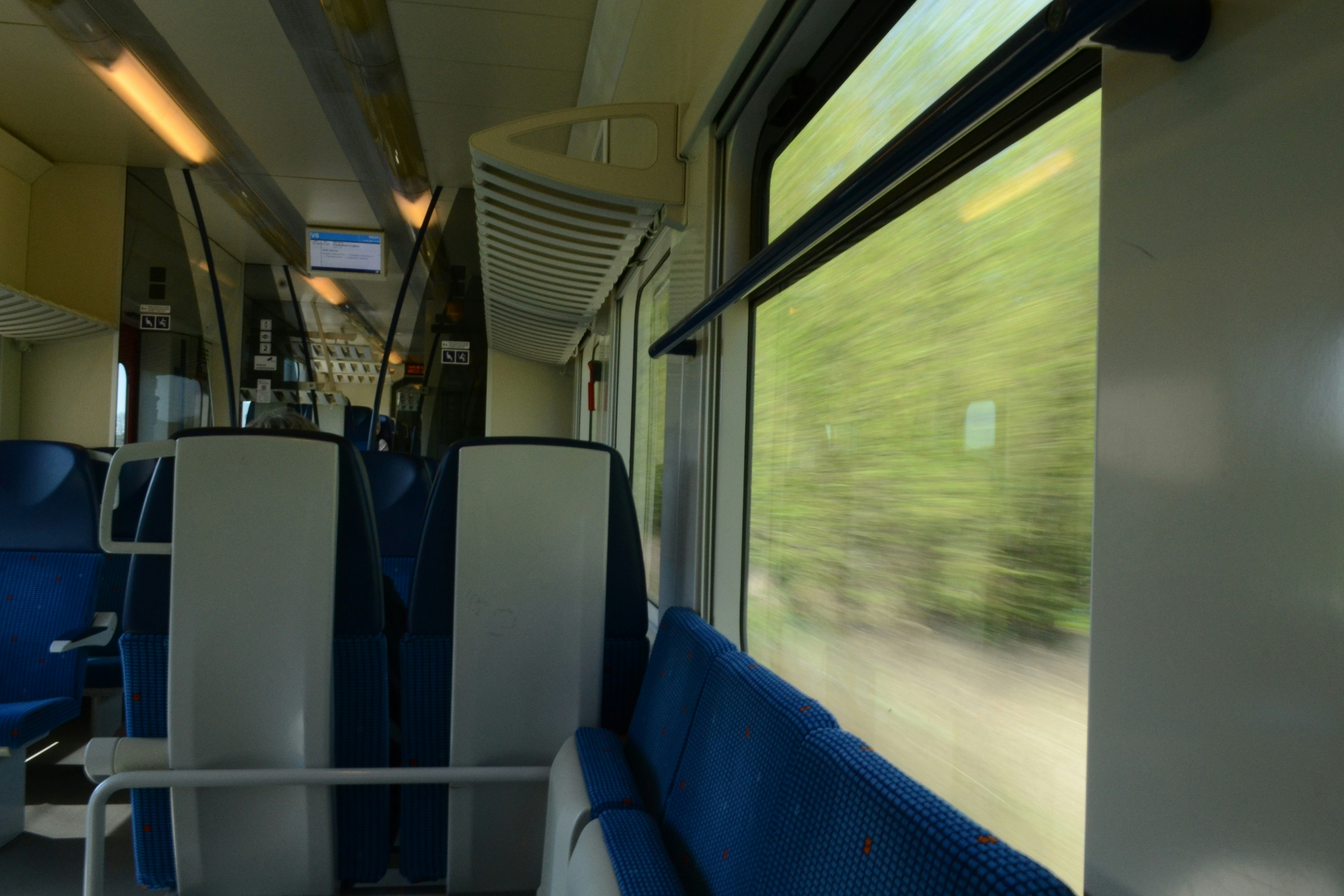 Interior kereta dengan kursi biru dan pemandangan yang lewat.