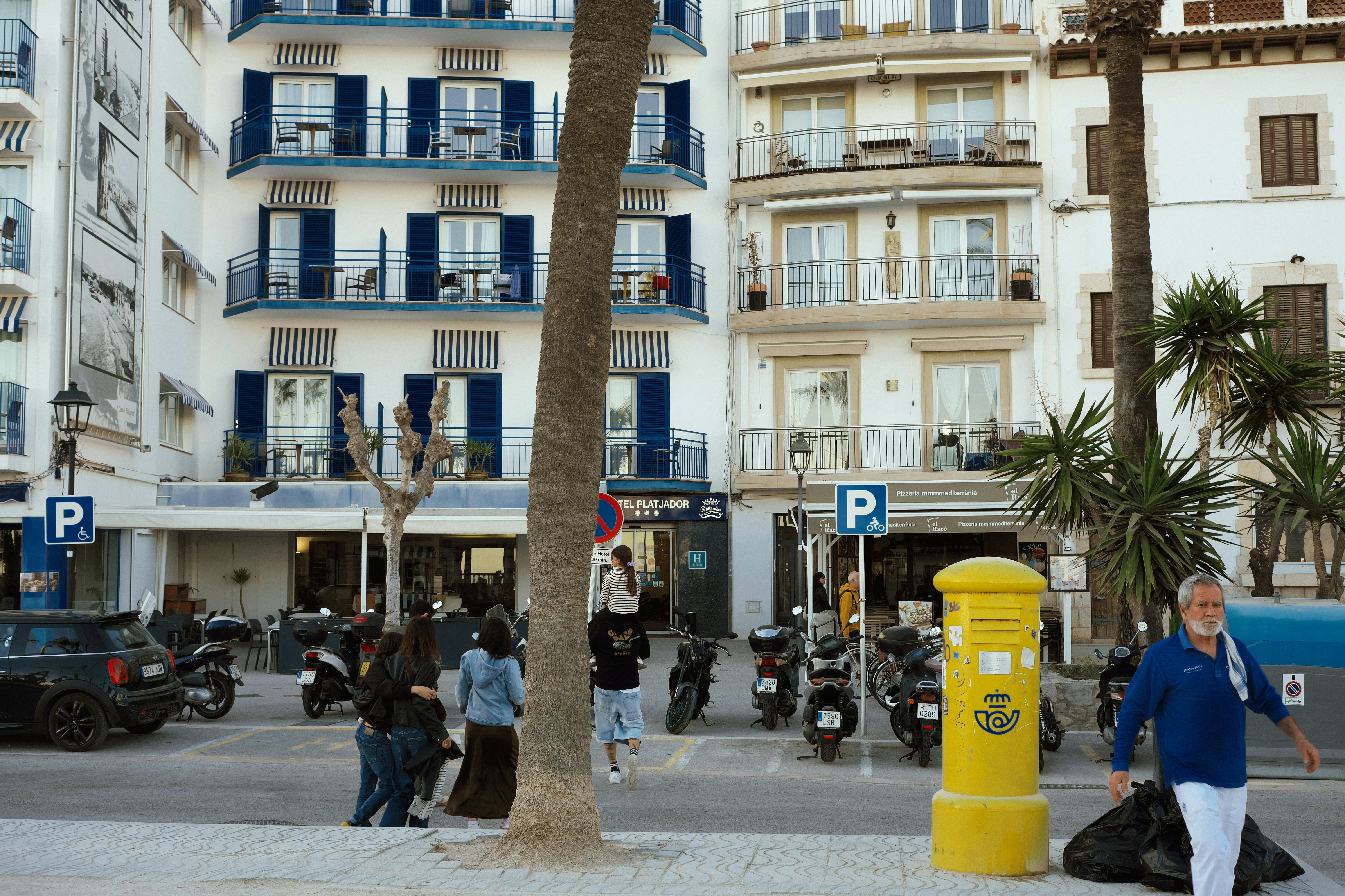 Pessoas passam por scooters estacionados e uma caixa de correio amarela.