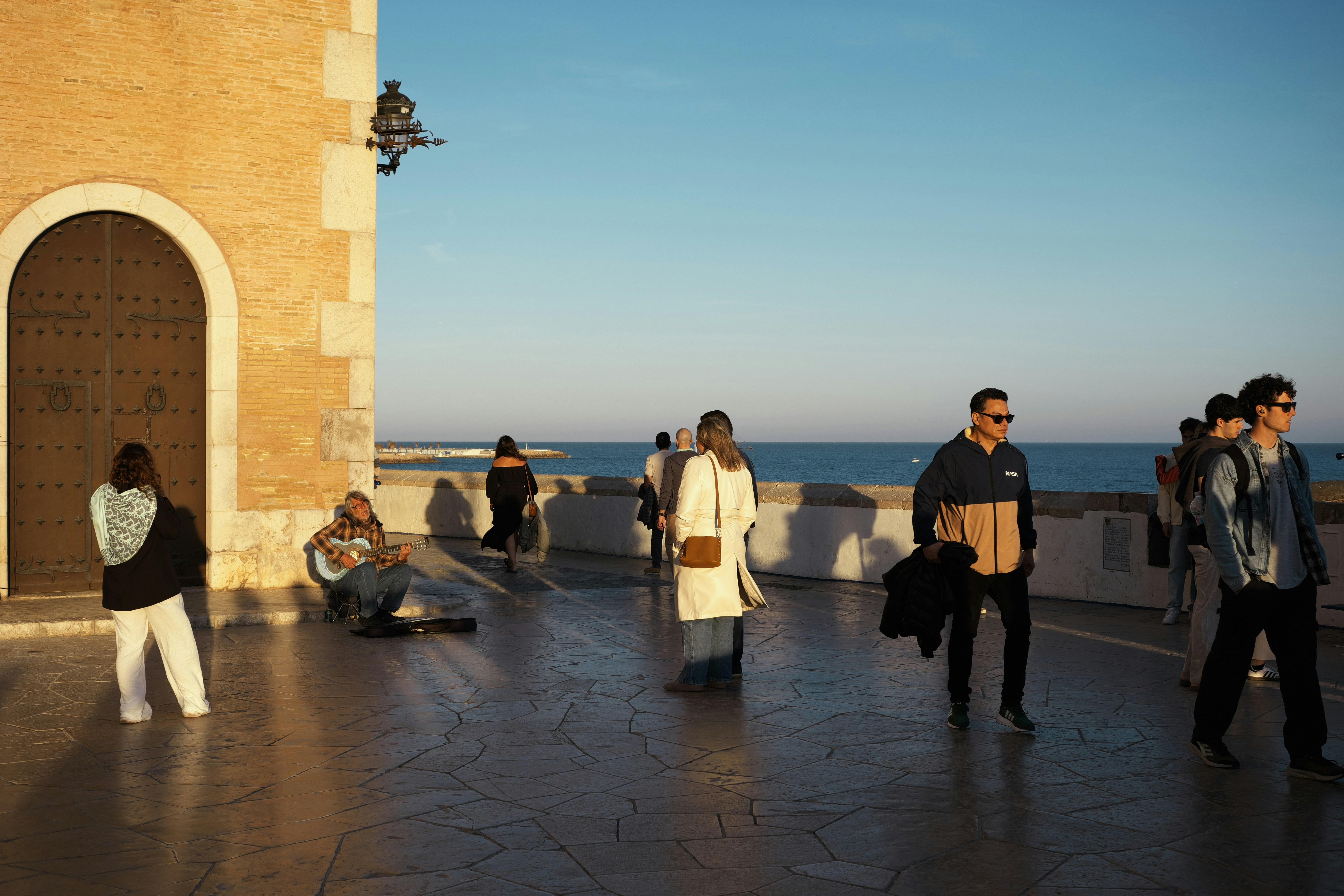 Pessoas caminhando por um calçadão ensolarado à beira-mar.