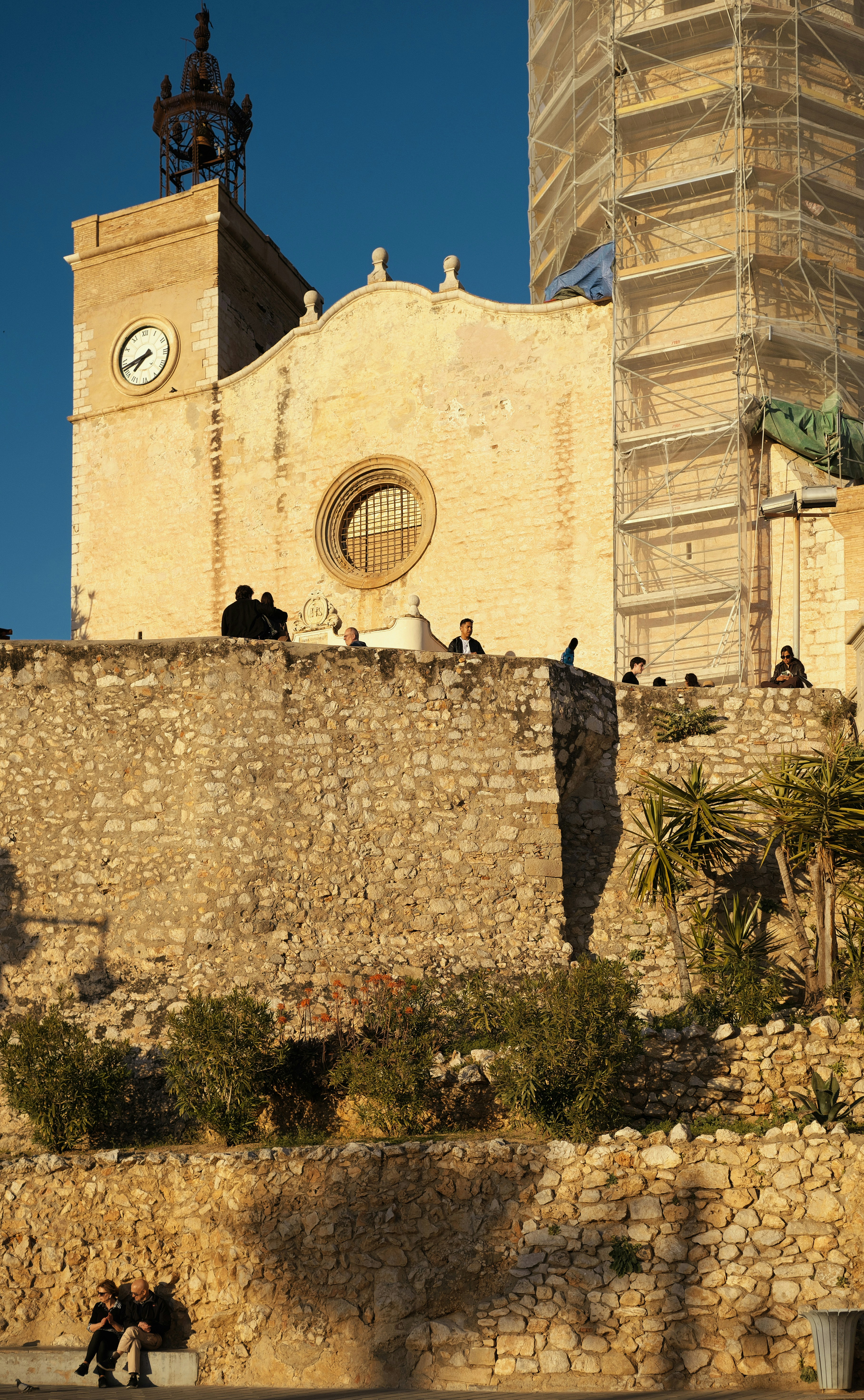 As pessoas se reúnem em um muro de pedra perto de uma igreja.