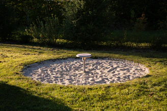 Circular sandbox with a play structure in grass