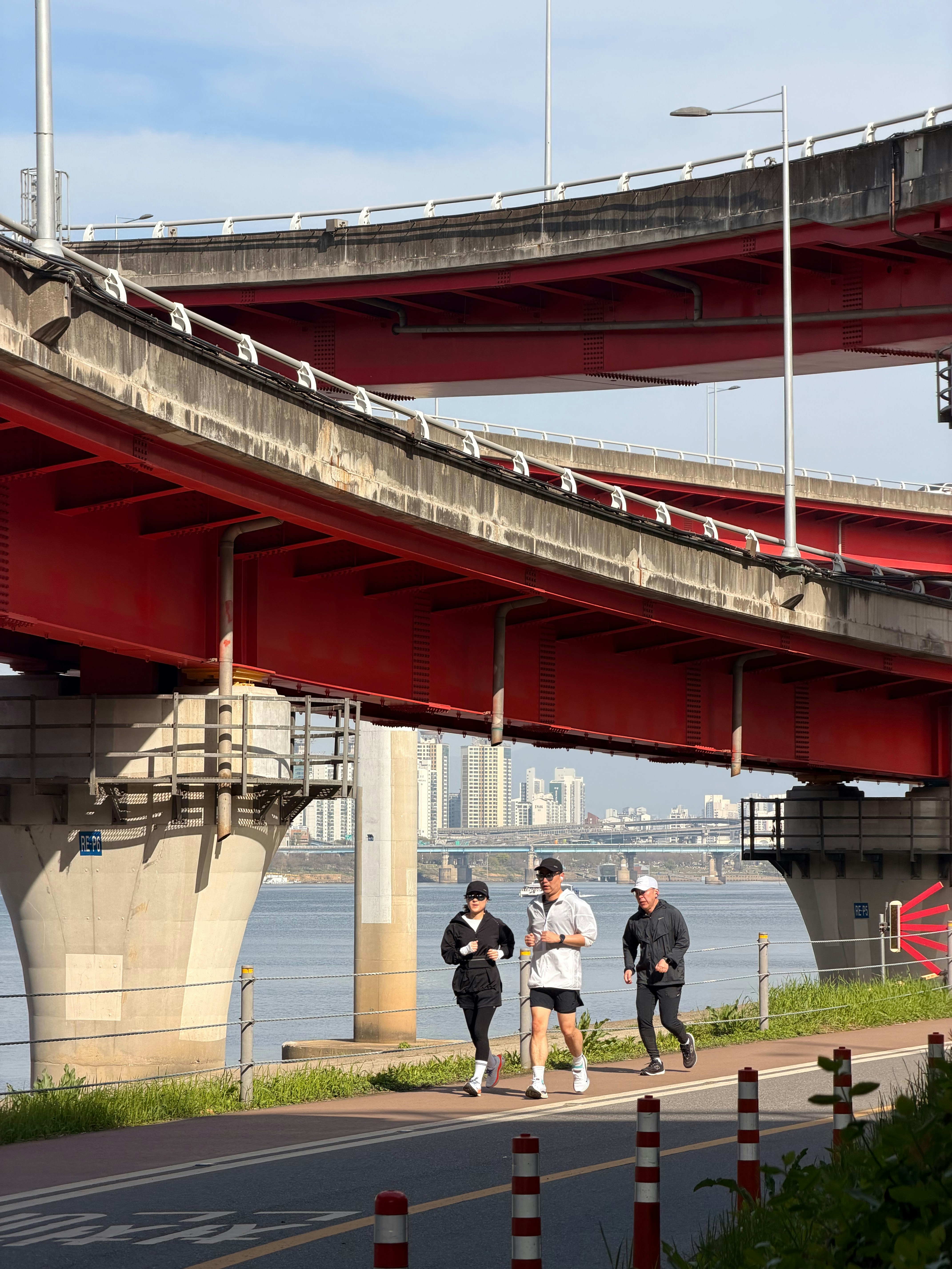 Three people jogging together along a waterfront path beneath bridges