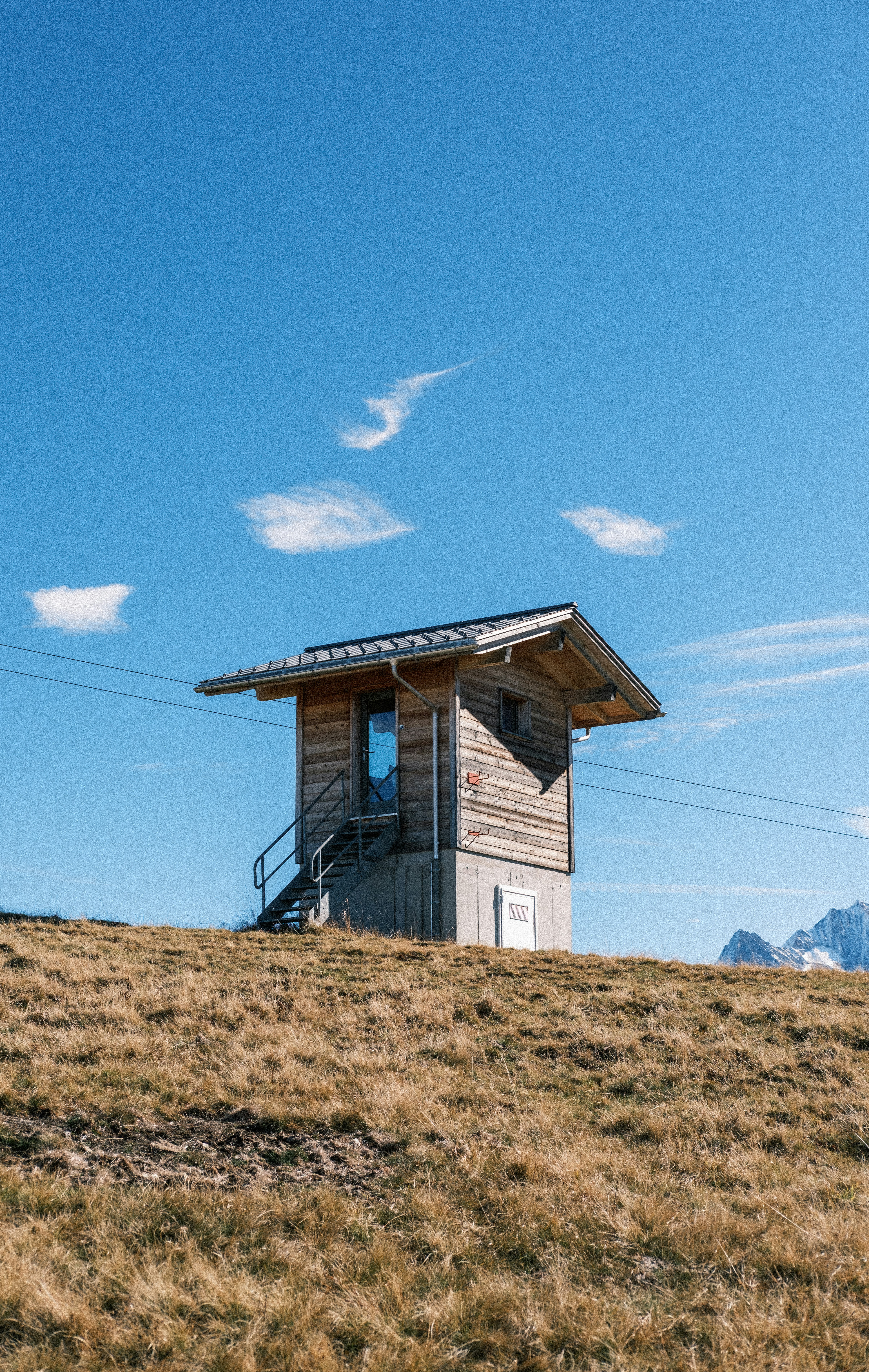 Kleine Holzhütte auf einem grasbewachsenen Hügel unter blauem Himmel