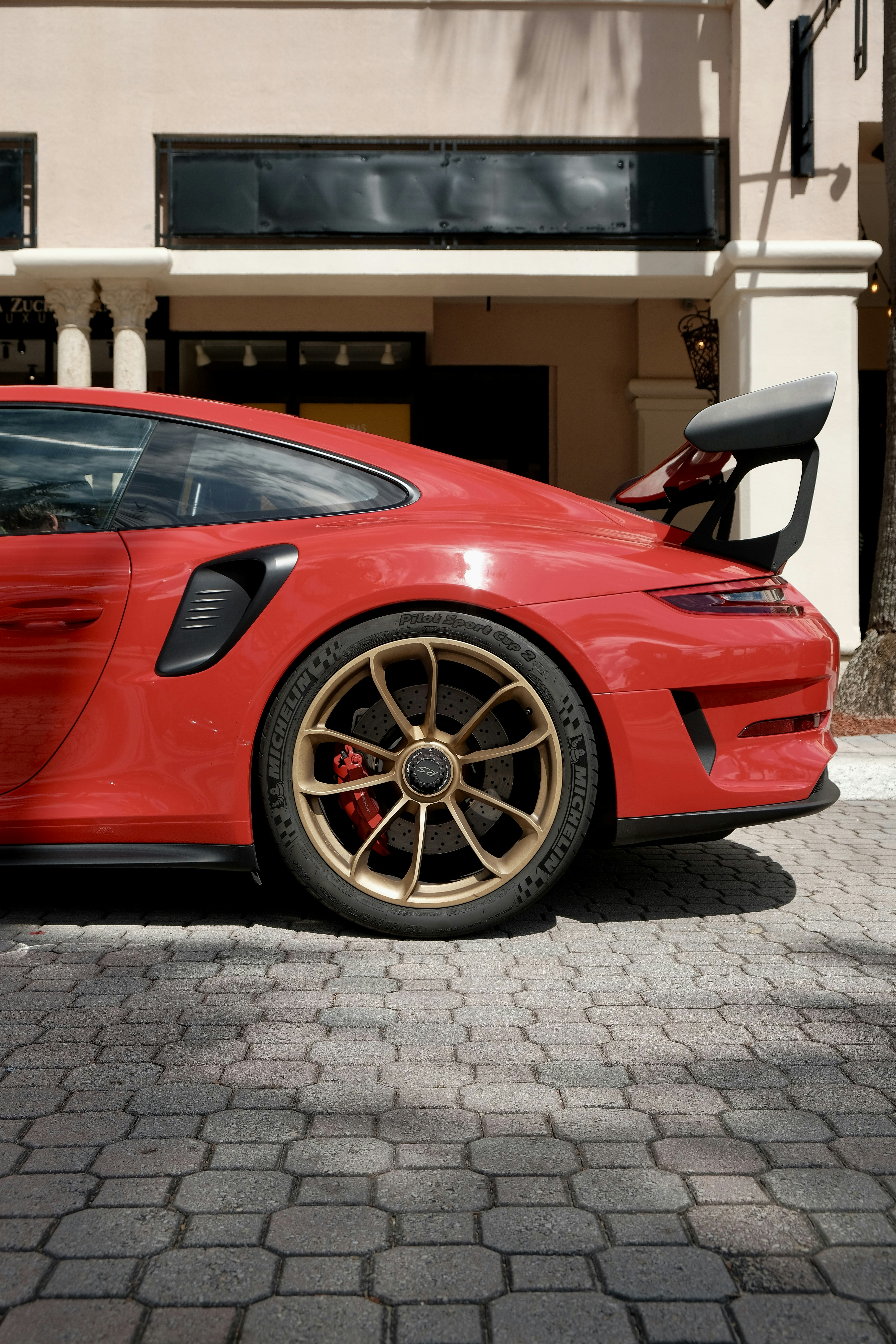 Auto sportiva rossa con ruote dorate parcheggiate su ciottoli.