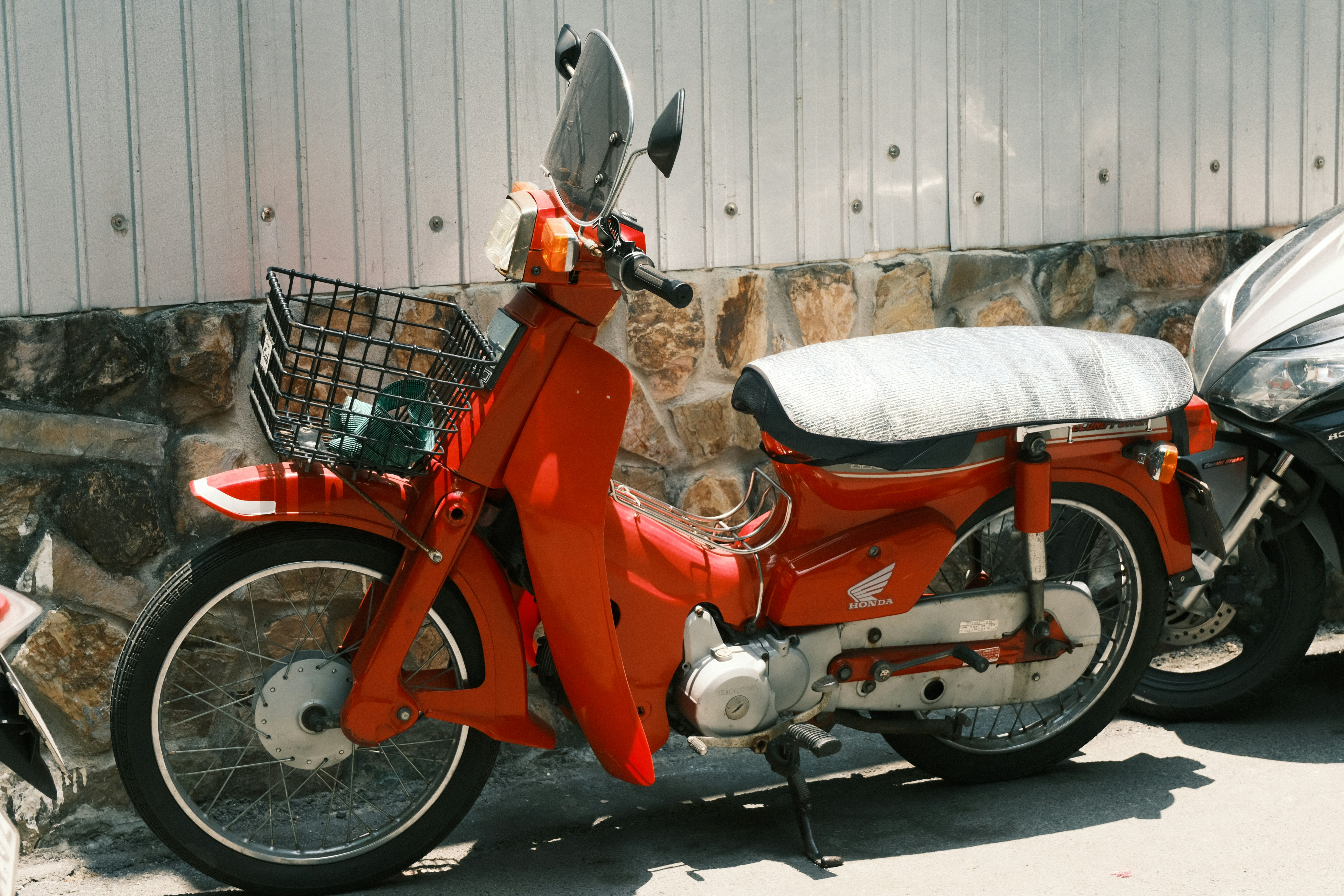 Uma scooter vintage laranja brilhante estacionada do lado de fora.
