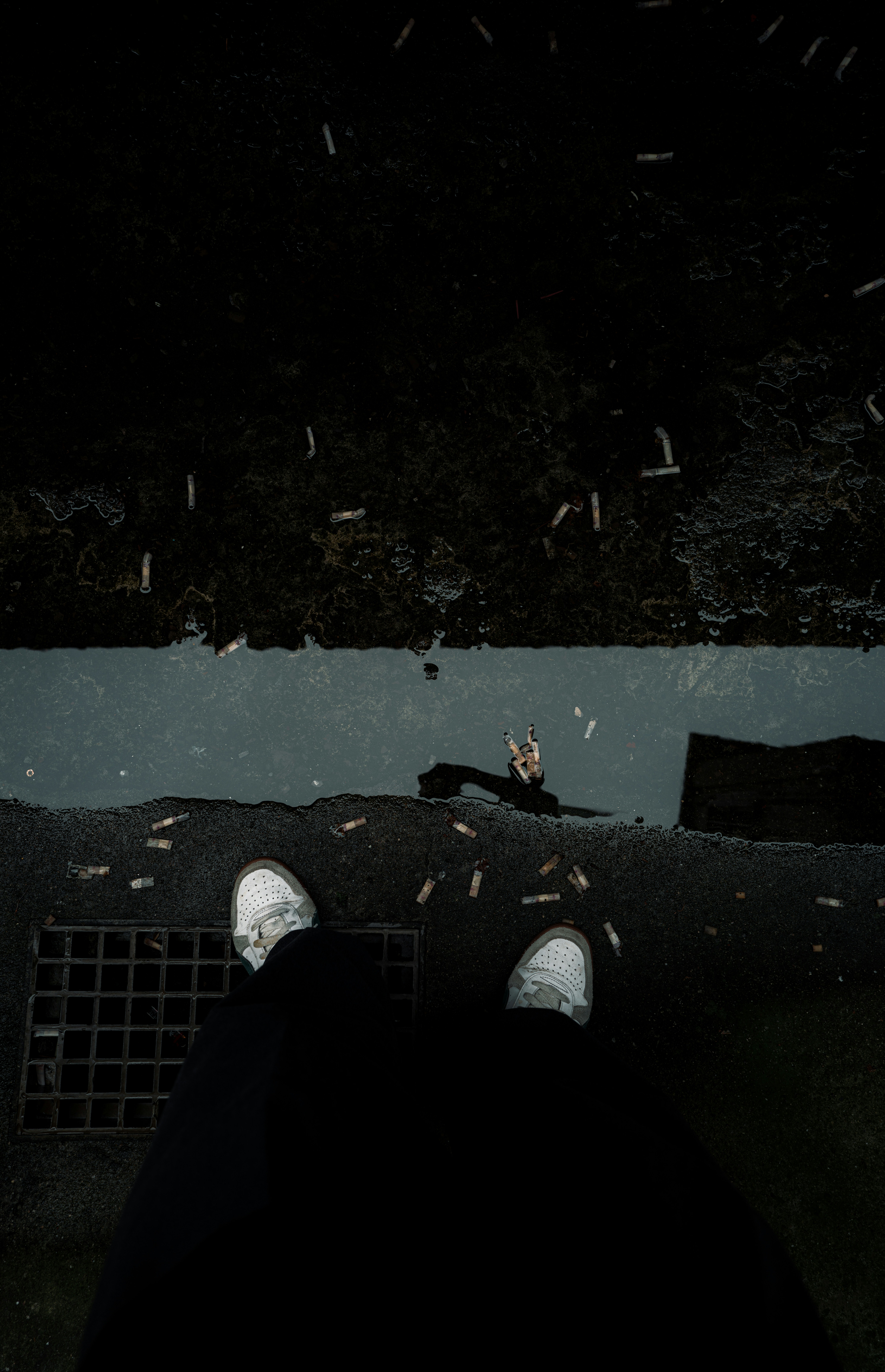 Uma pessoa está em pé em uma rua molhada com bitucas de cigarro.