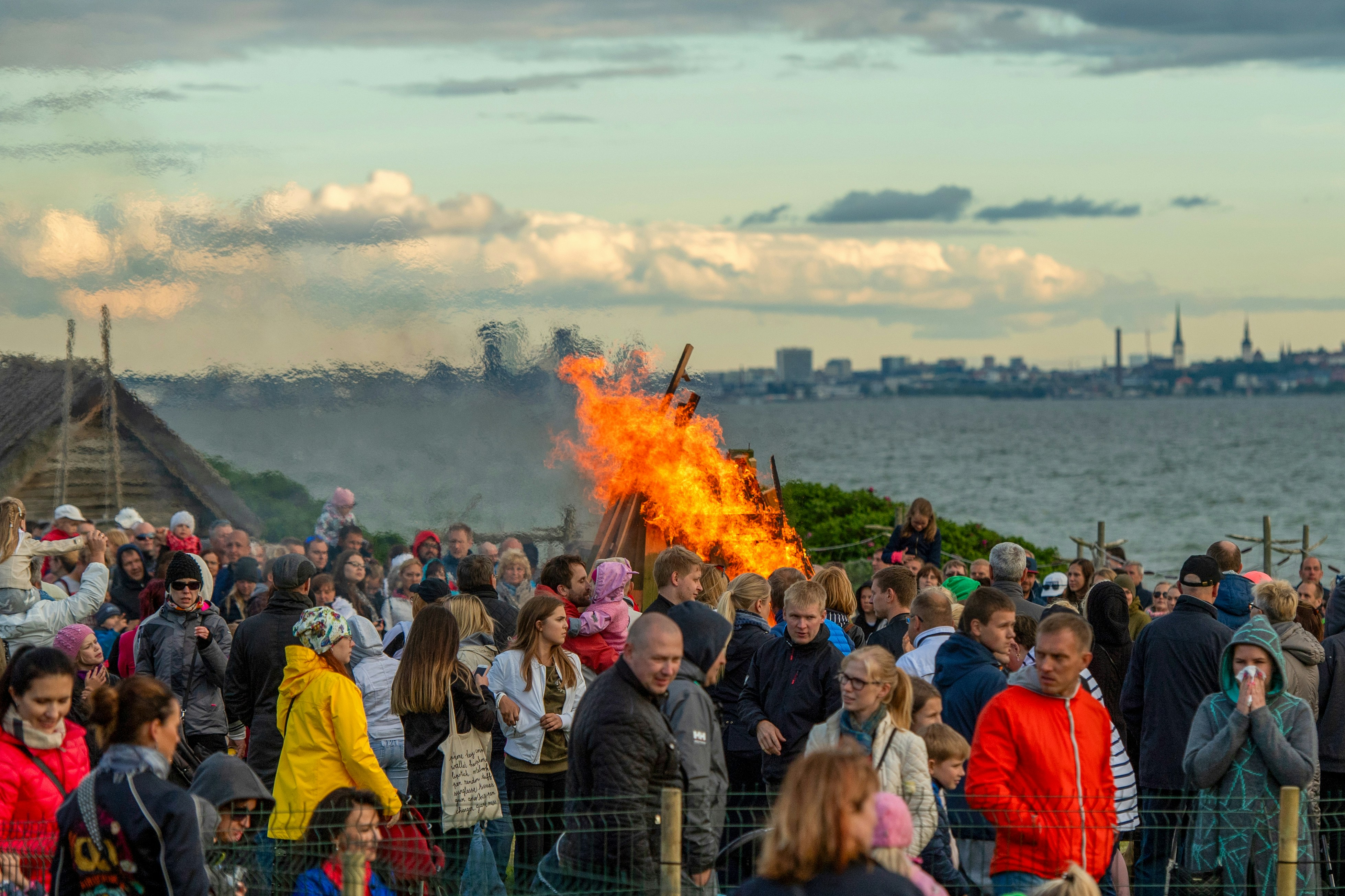Crowd watches large bonfire by the sea at dusk