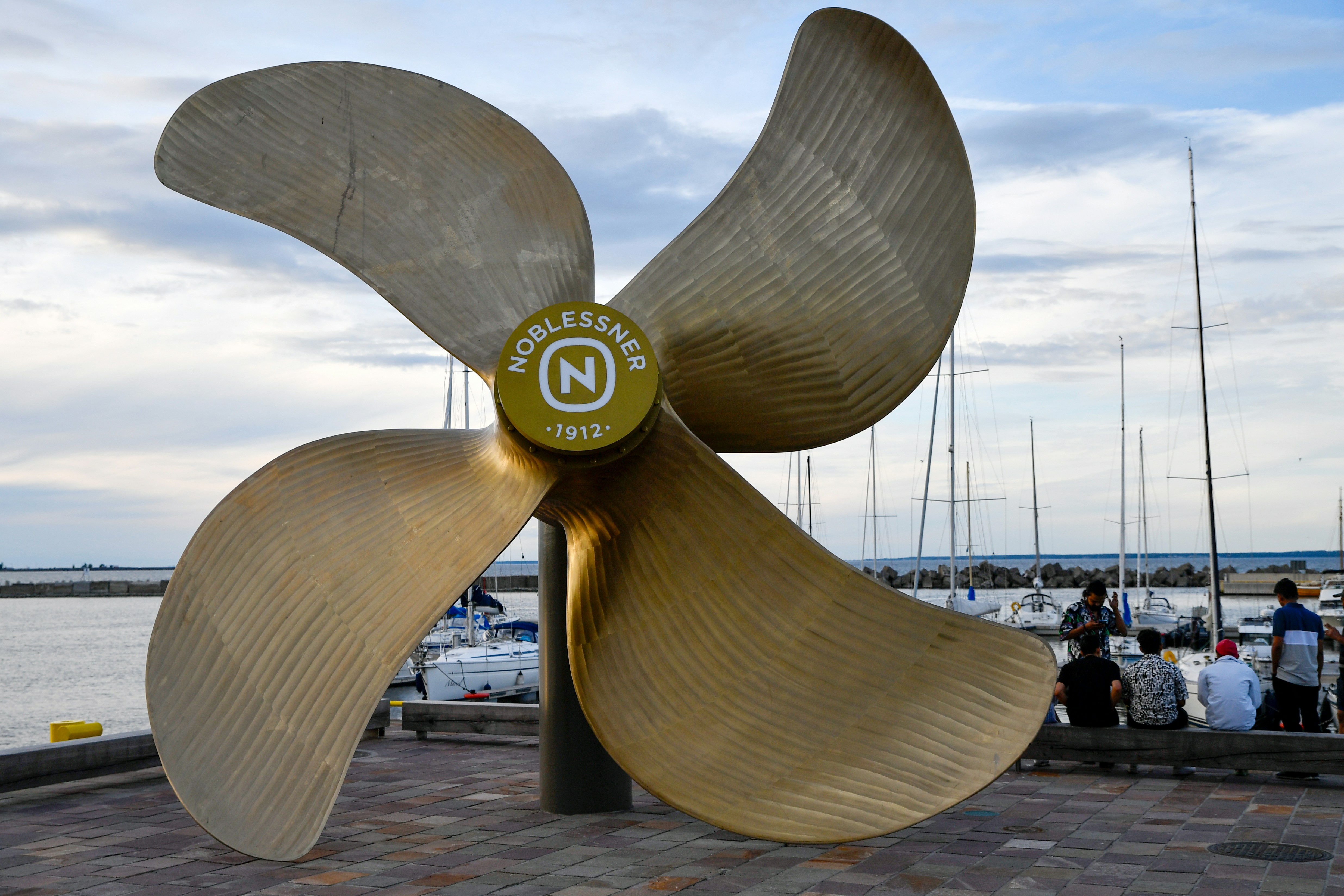 "A monumental bronze ship propeller sculpture at the historic Noblessner marina in Tallinn, Estonia, standing as a tribute to the district's submarine shipbuilding heritage against a backdrop of modern yachts."