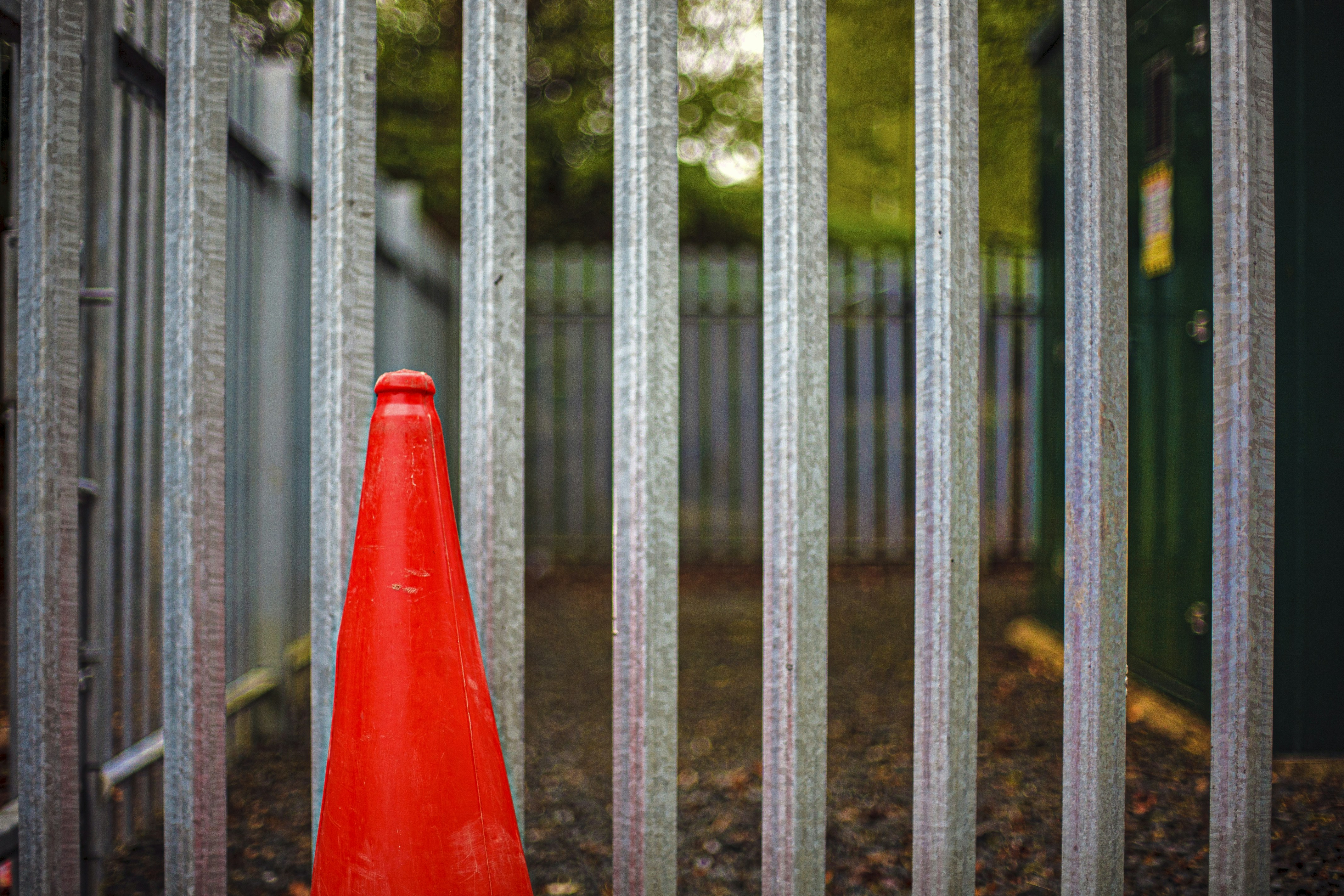 Um cone de trânsito laranja brilhante atrás de uma cerca de metal.