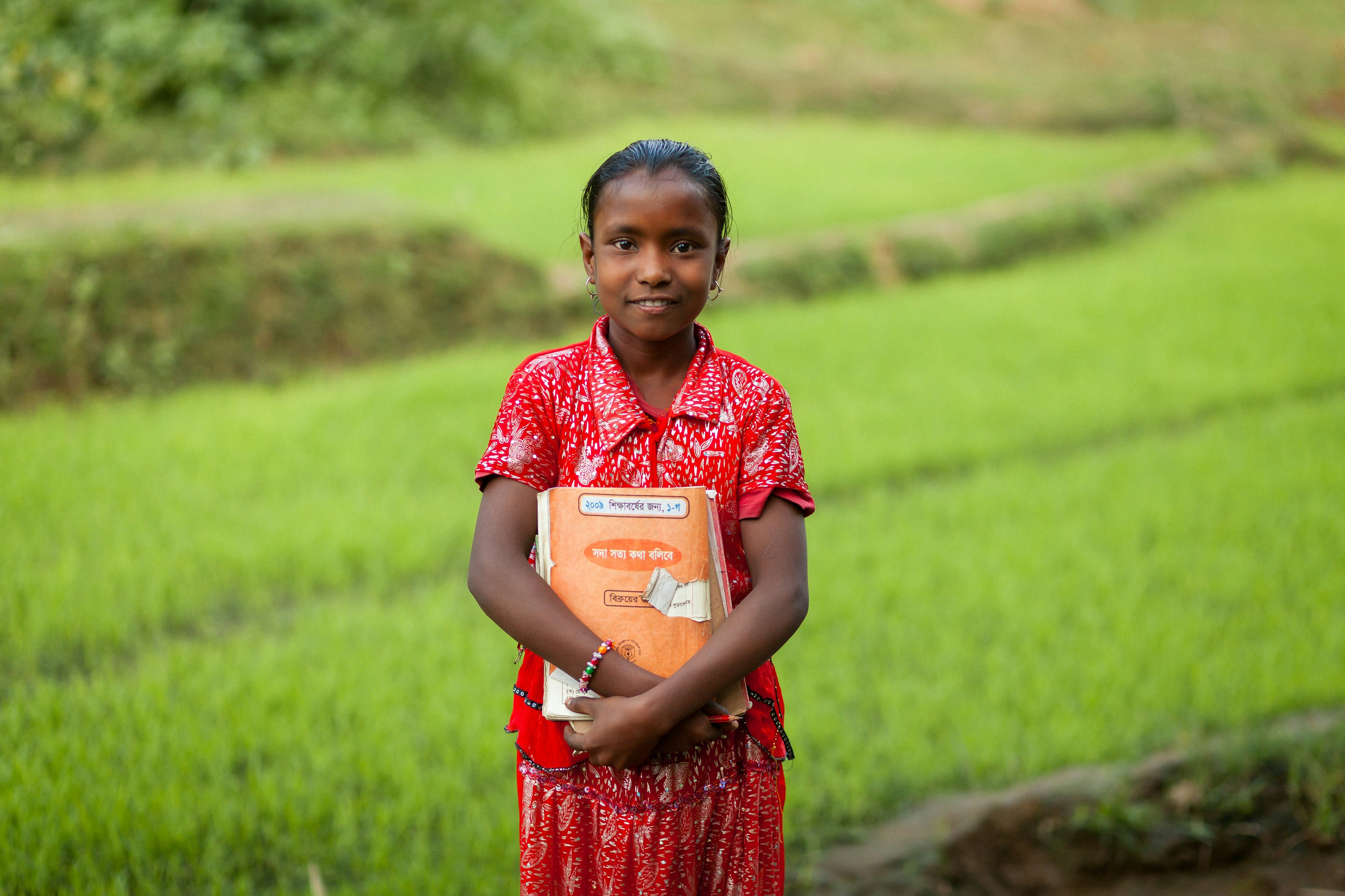 Young girl in traditional clothing holds a book outdoors.