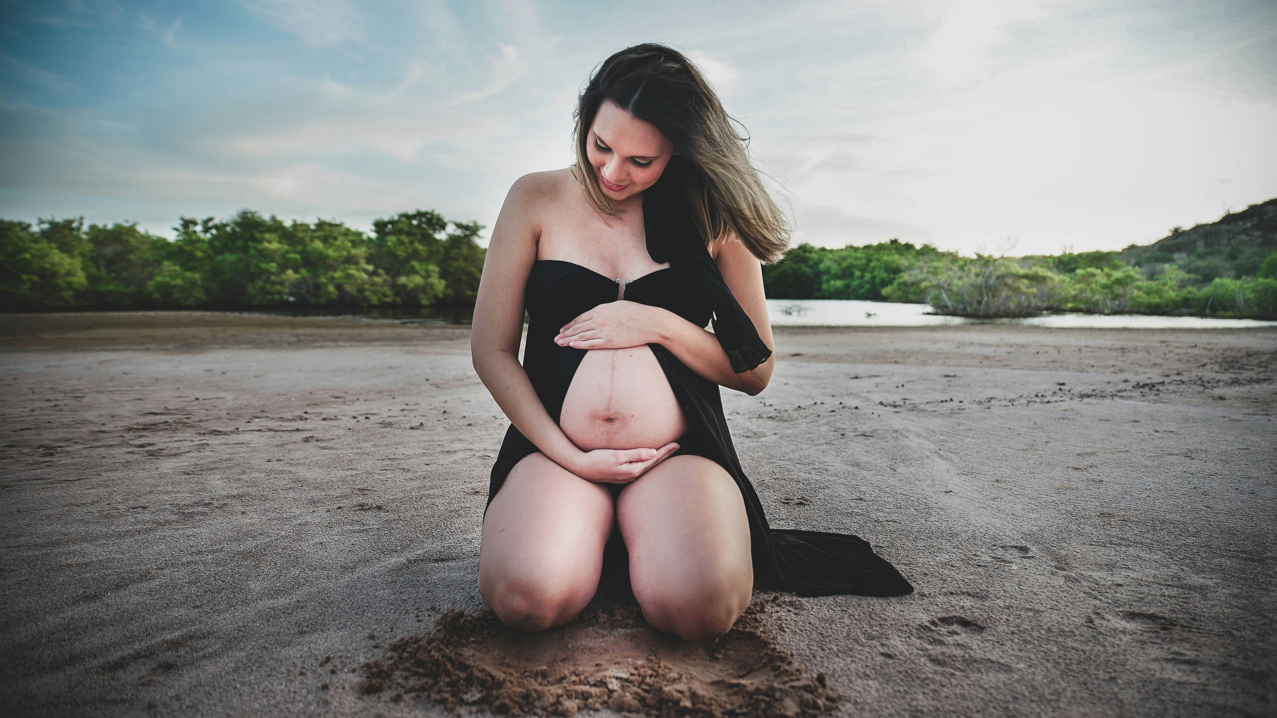 Donna incinta inginocchiata su una spiaggia sabbiosa