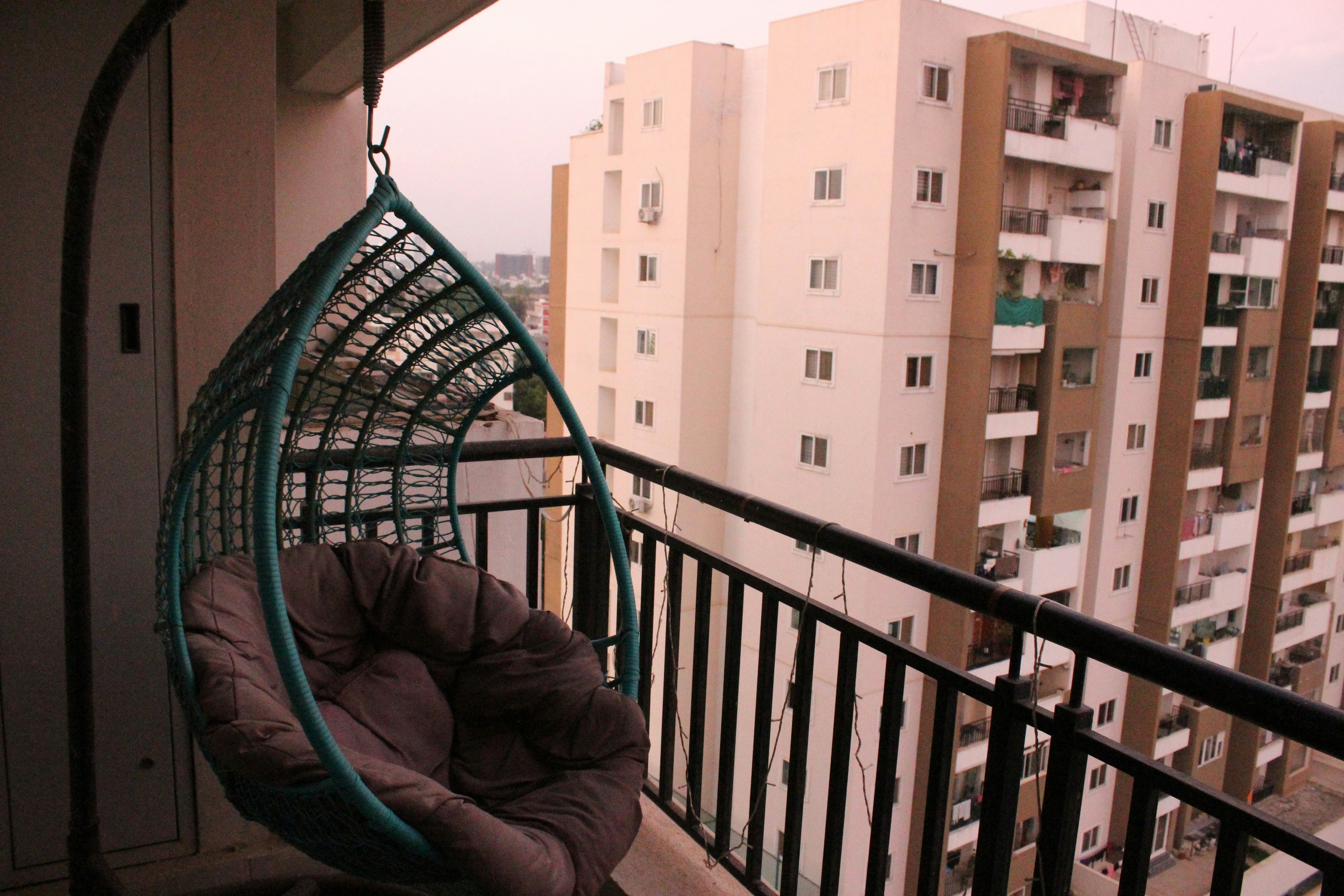 Teal hanging egg chair on a small apartment balcony overlooking city buildings