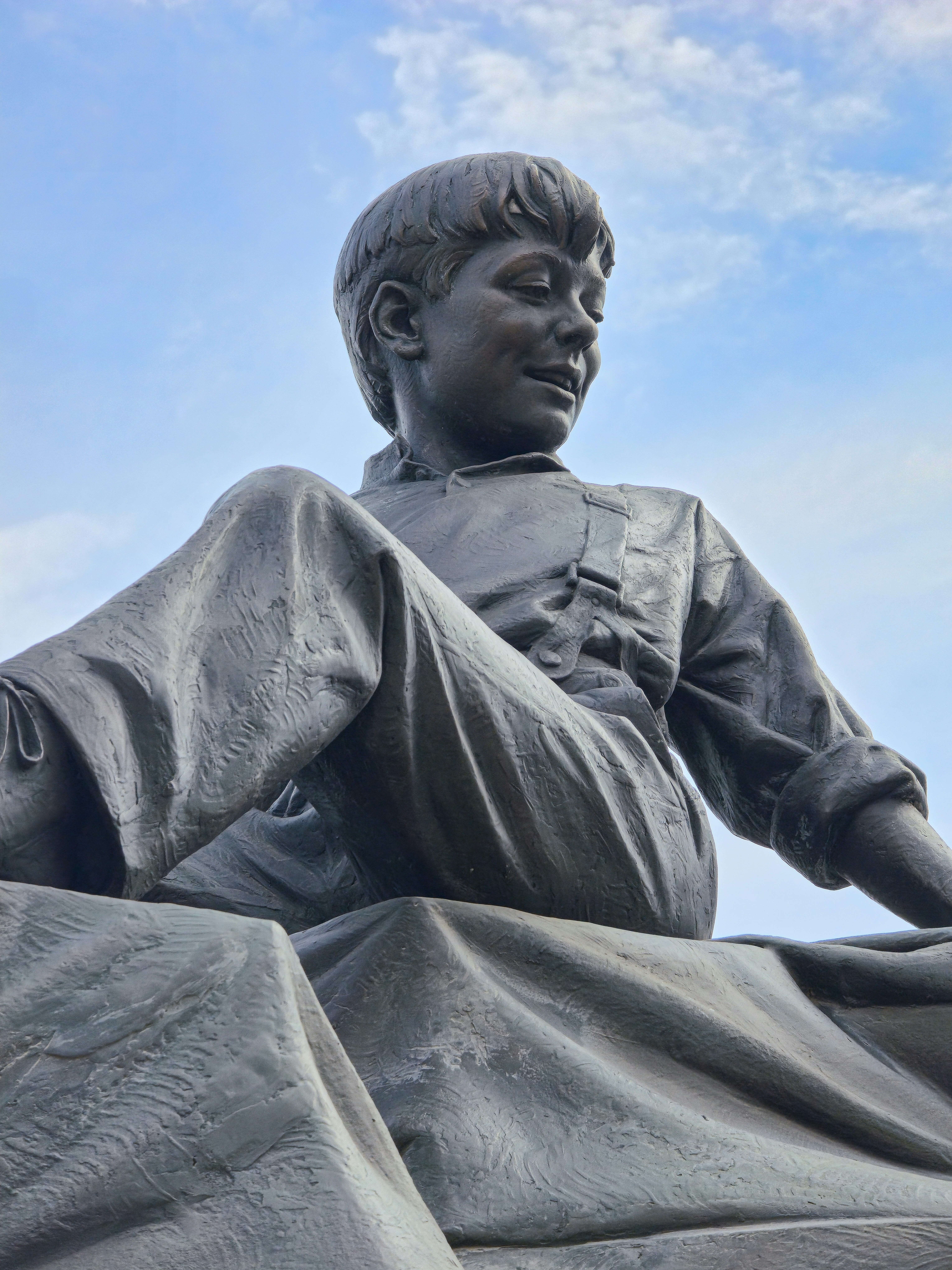 Eine Bronzestatue eines jungen Jungen, der draußen sitzt.