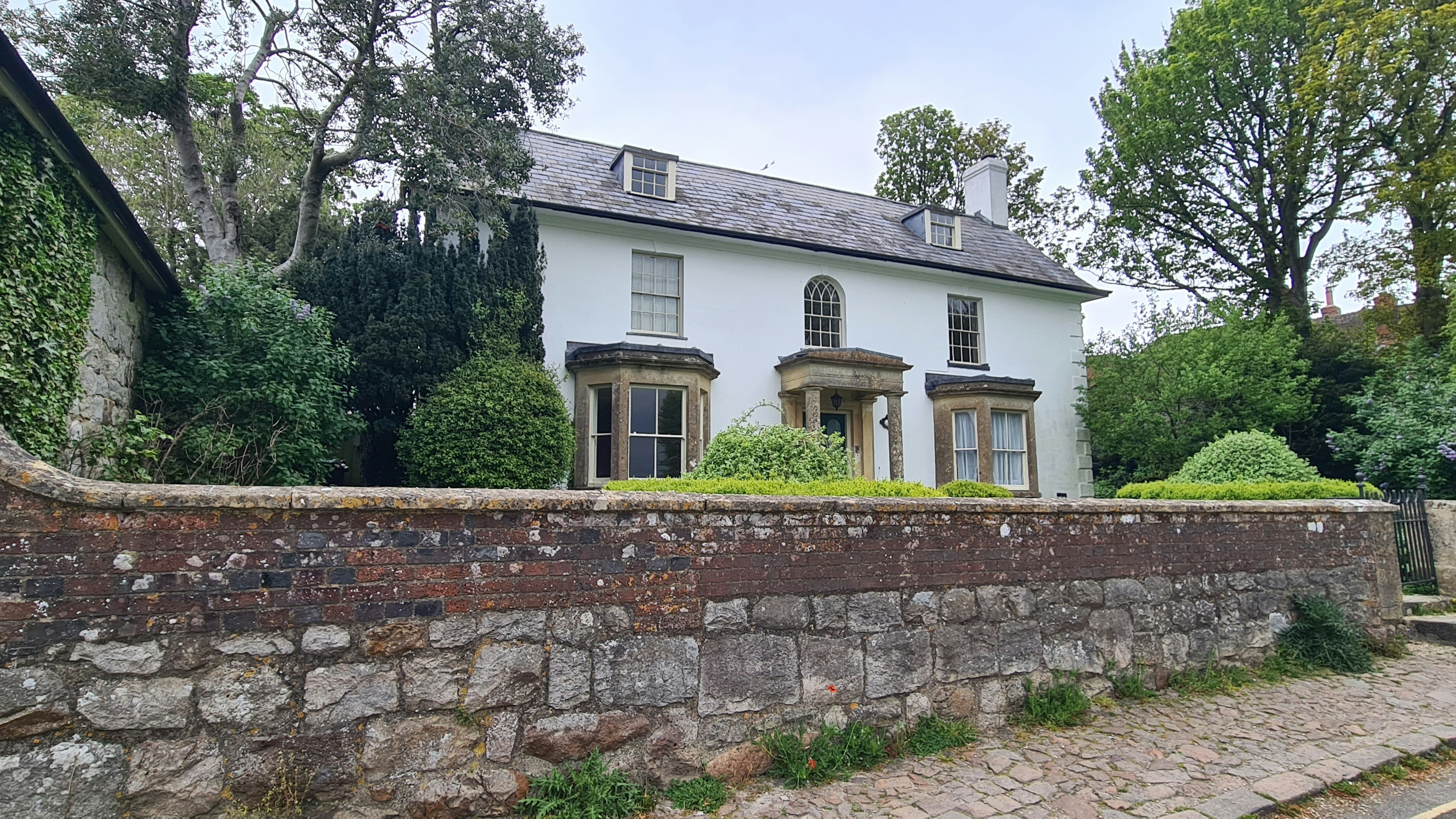 A white house behind a stone wall and trees