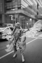 Woman in elaborate costume with wings dances in street.