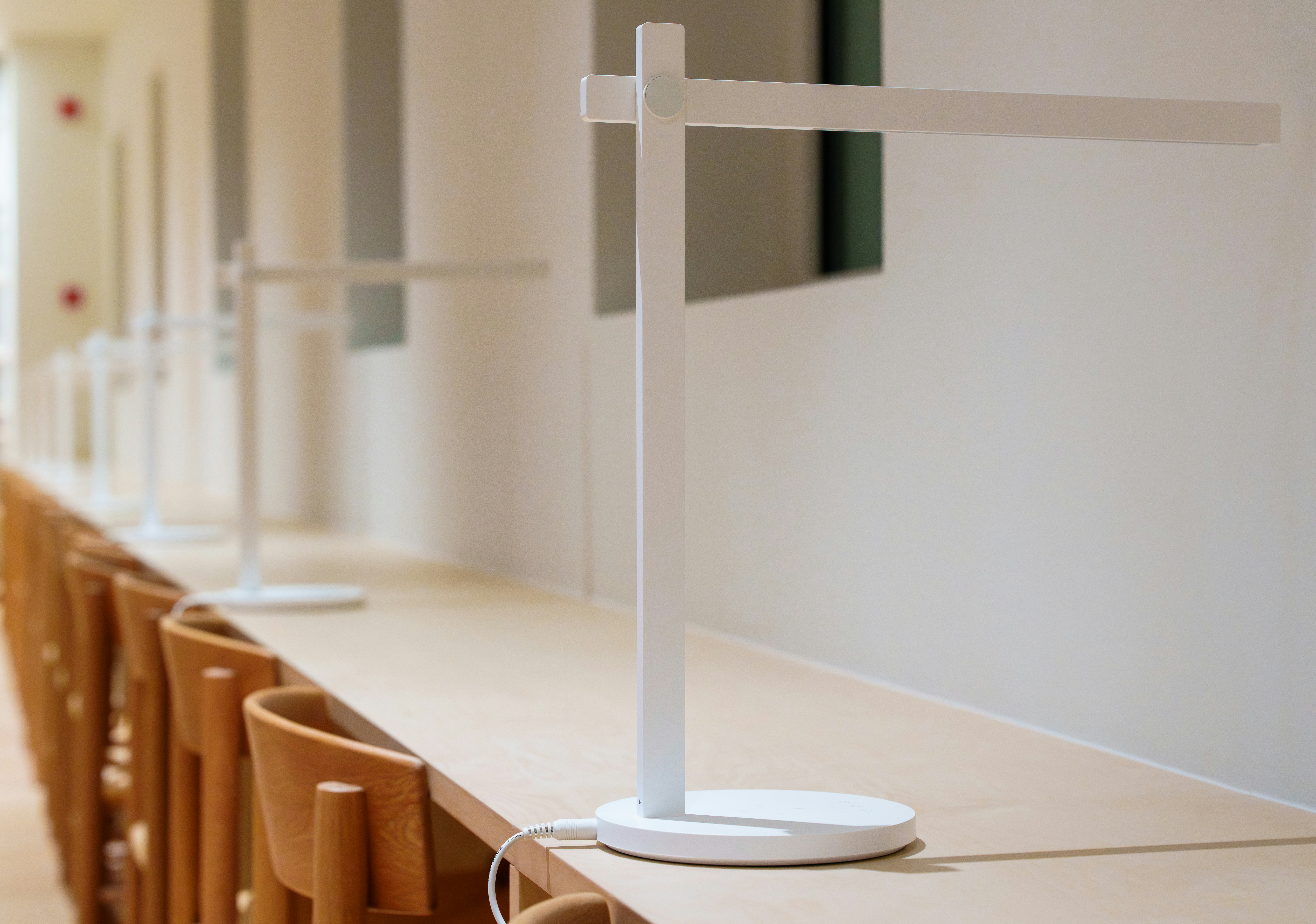 Modern white desk lamps on a long wooden table.