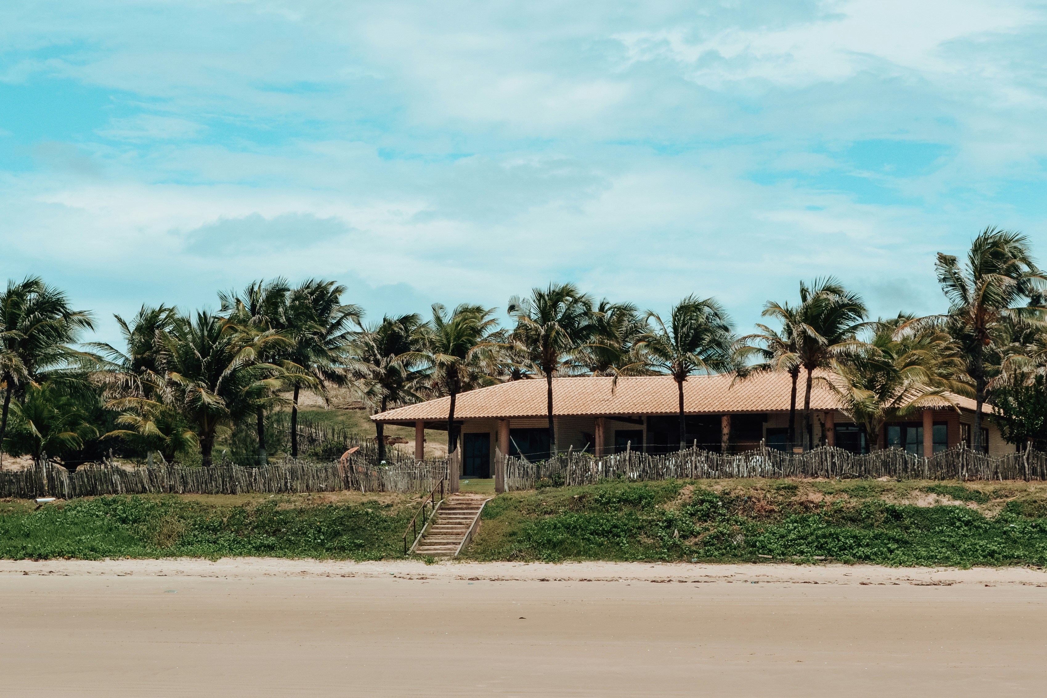 Maison de plage entourée de palmiers sous un ciel nuageux.