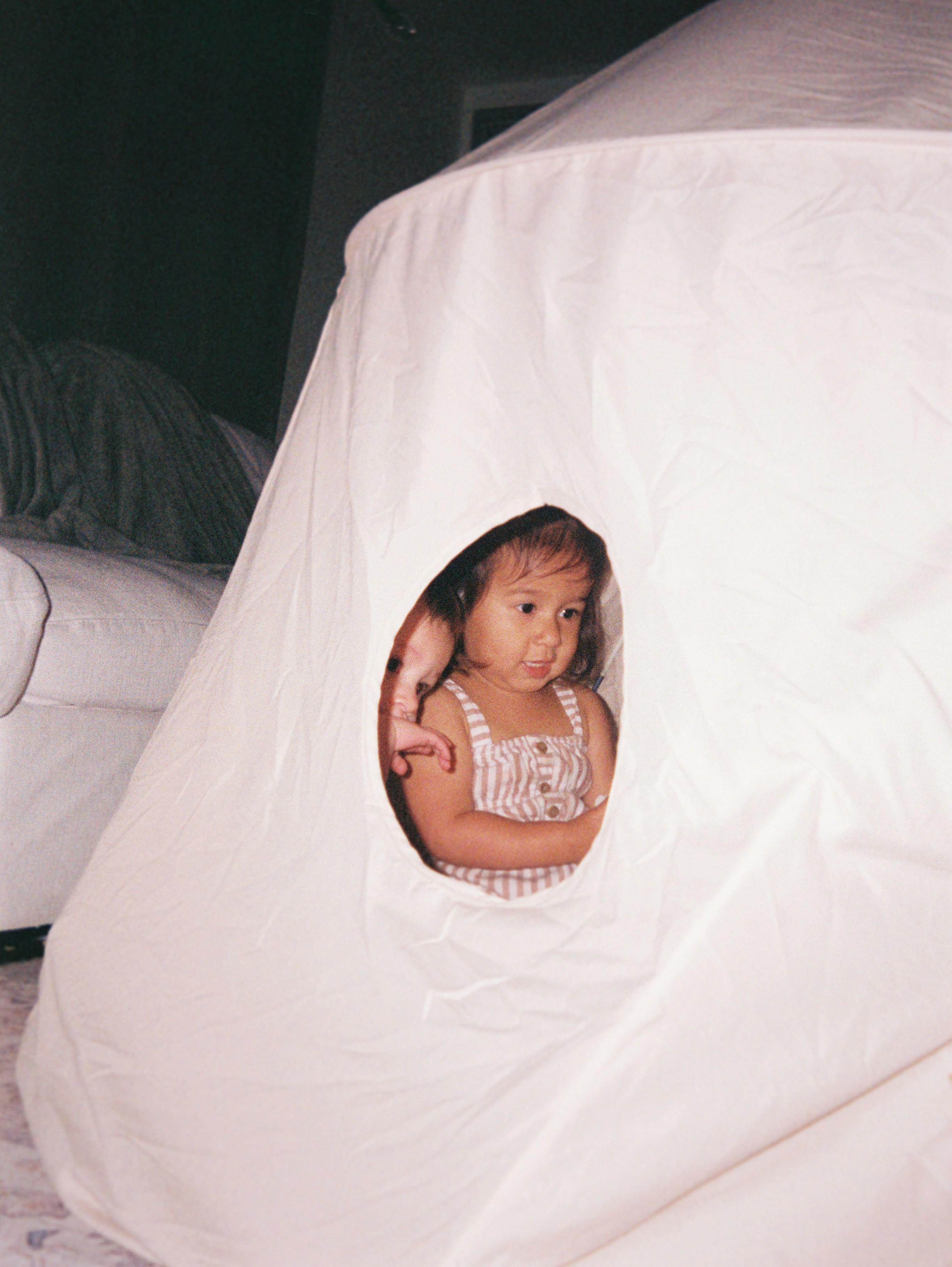 A young child peeking from a white play tent.