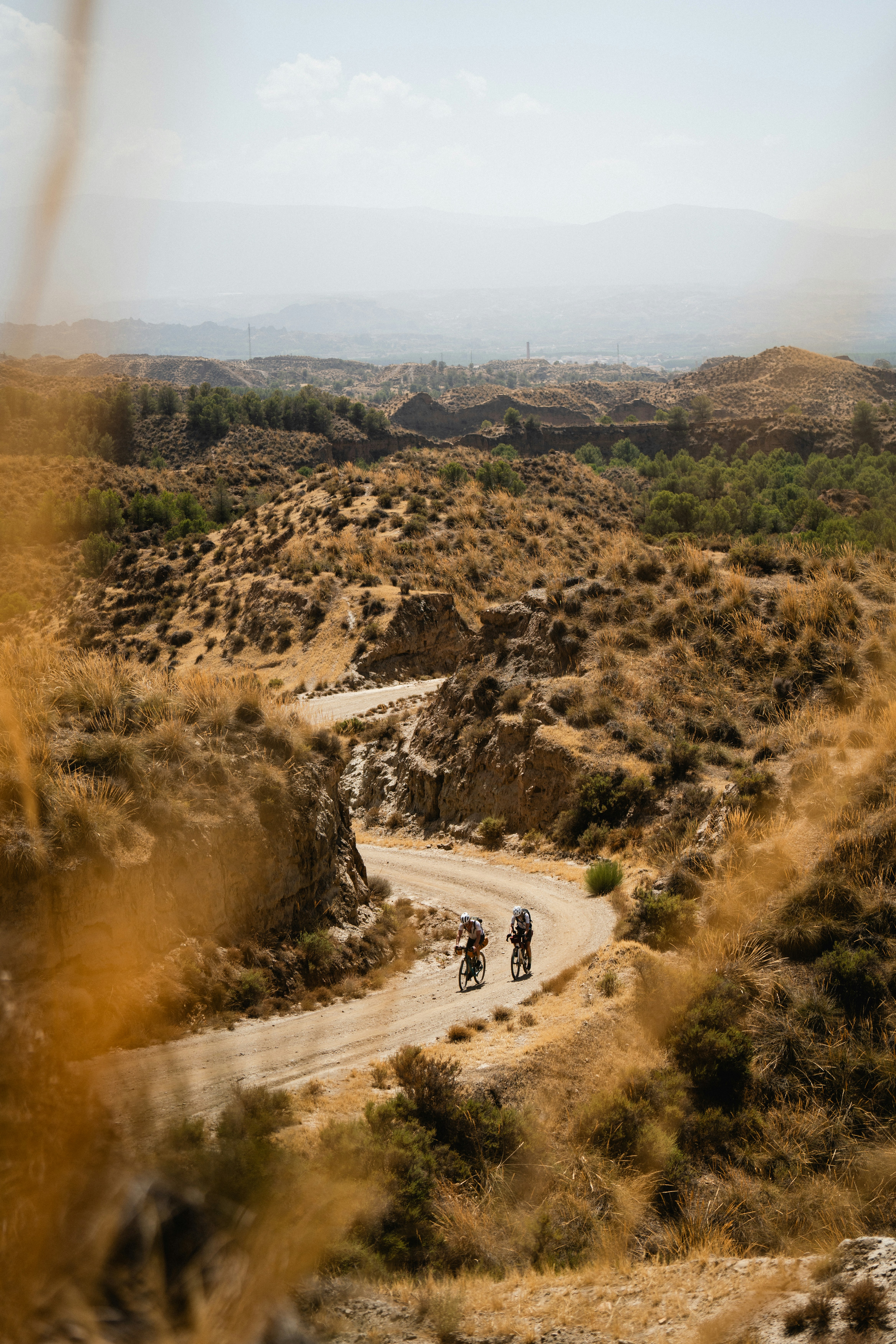 Two cyclists on a winding dirt road through dry hills.