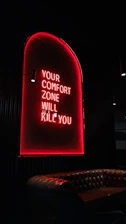 Red neon sign reads "your comfort zone will kill you".