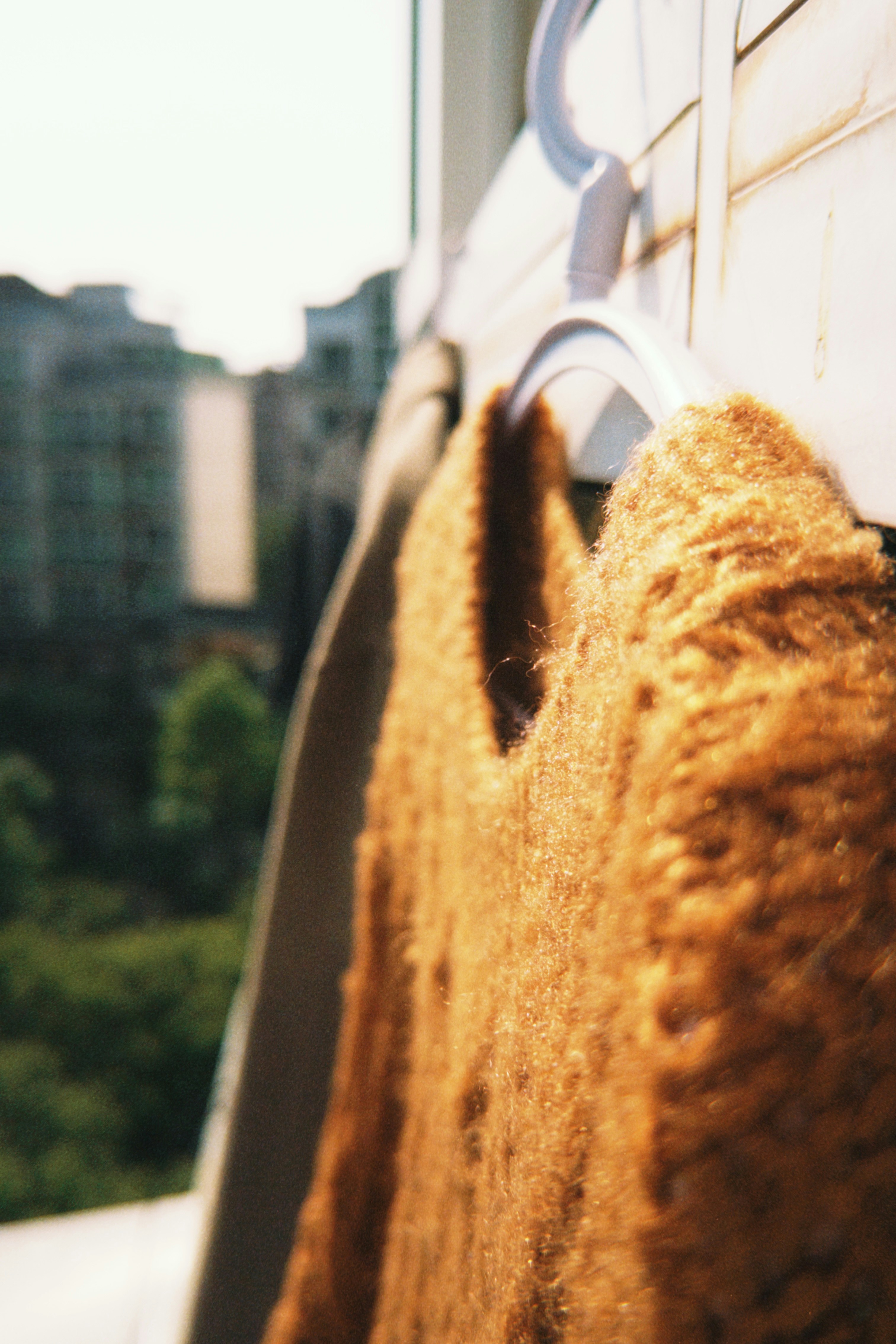 A fuzzy brown sweater hangs on a hanger outside.