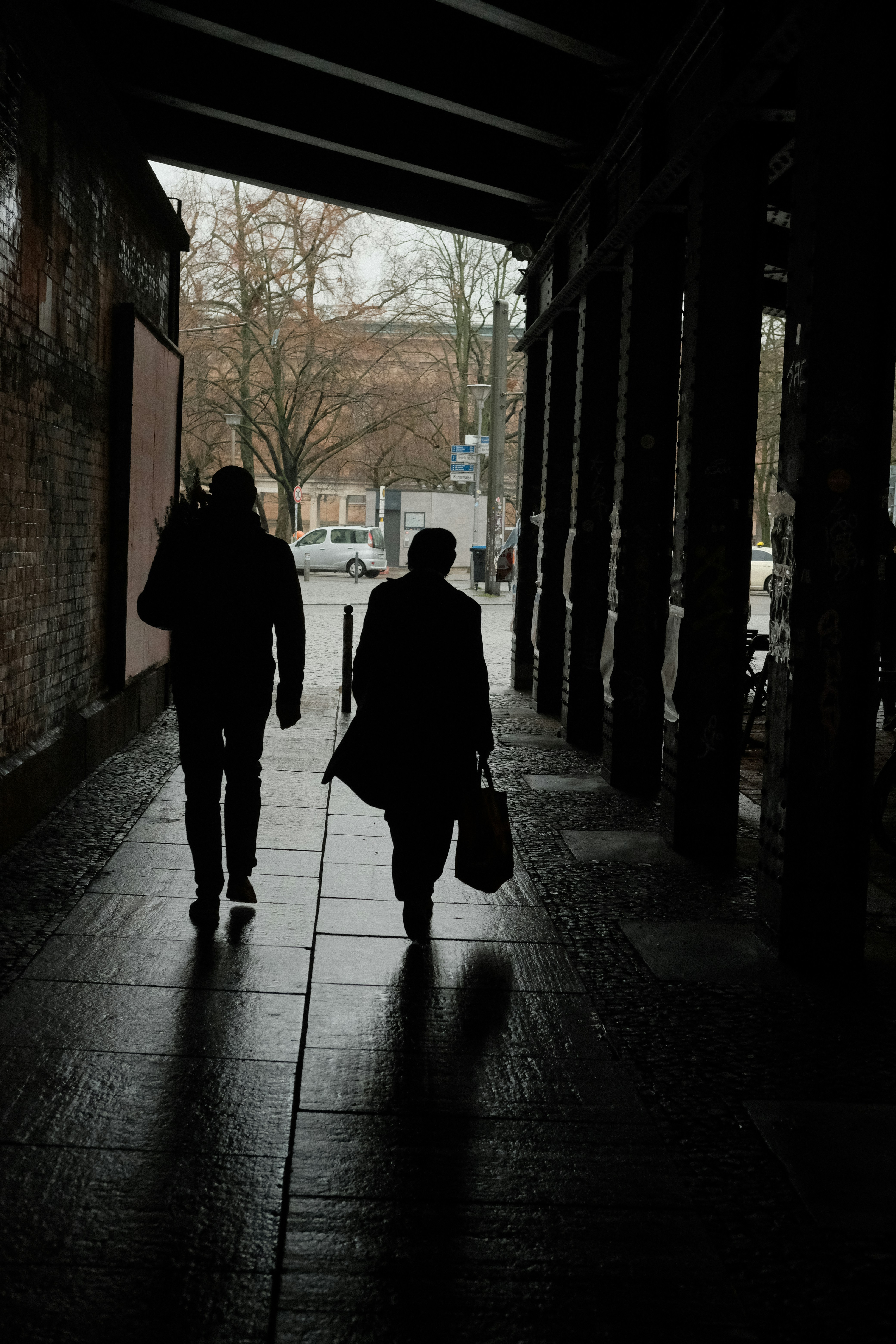 Two people walk down a dark, covered walkway.