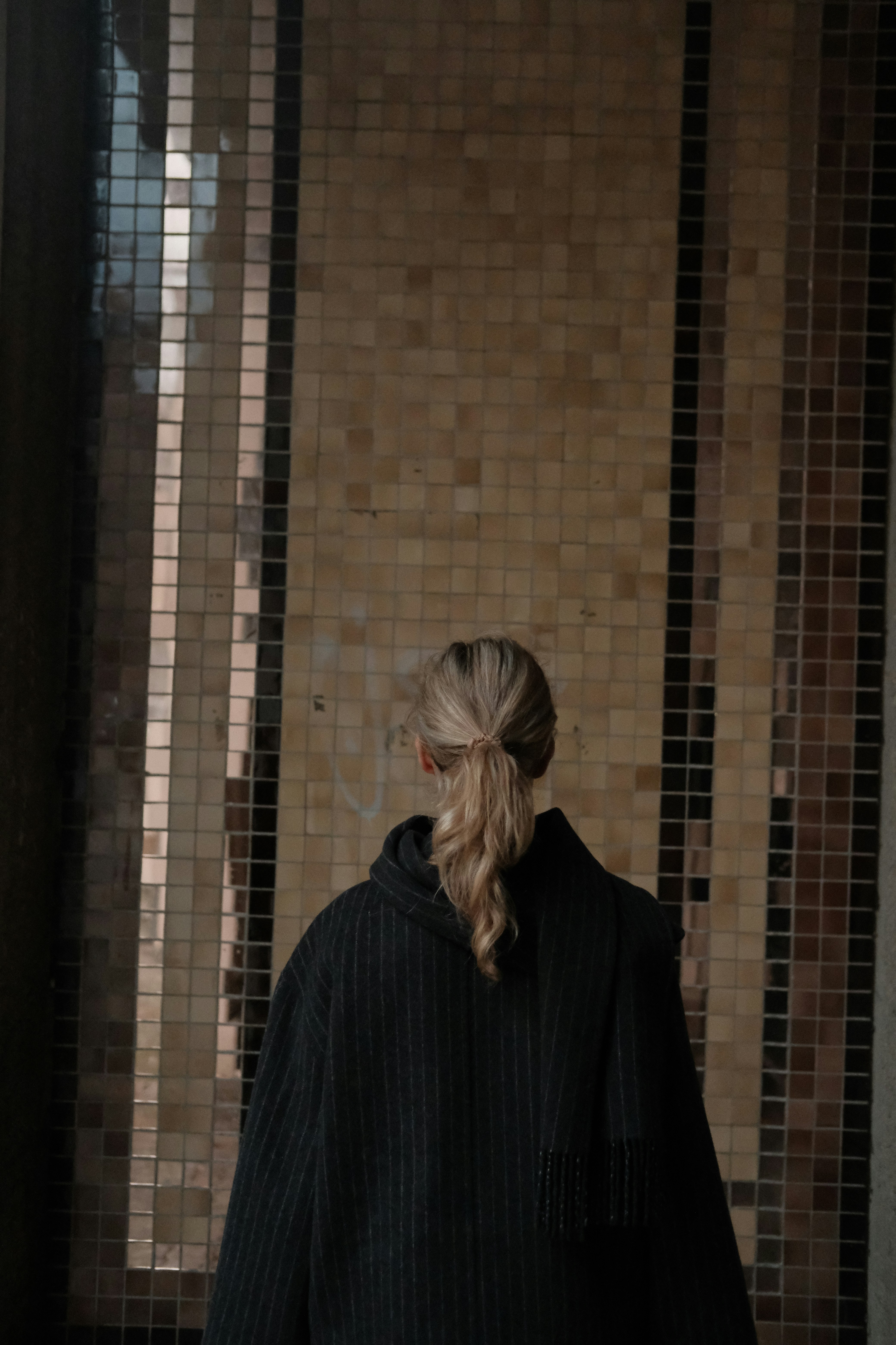 Woman with ponytail in striped coat facing mosaic wall