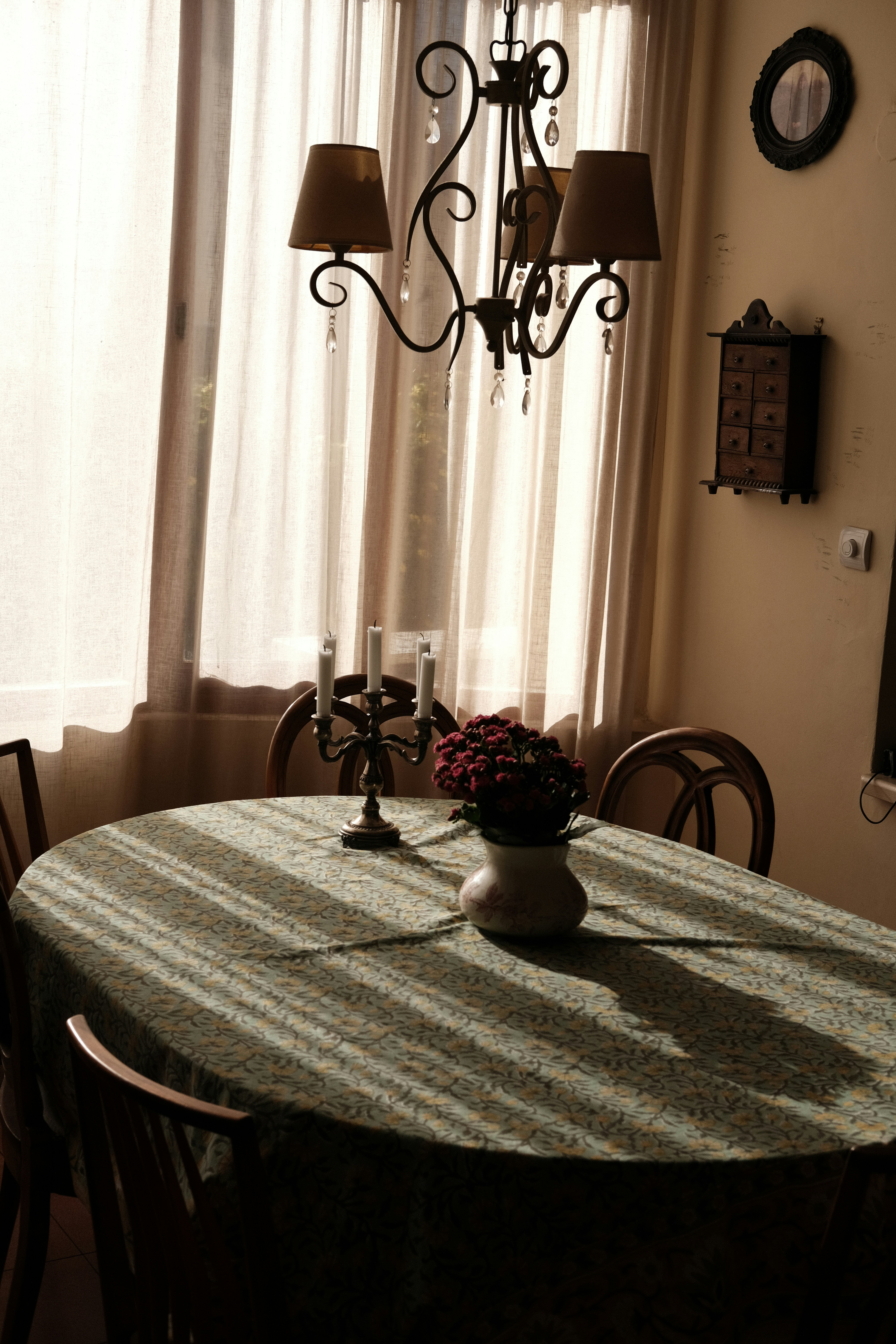 Dining table with chandelier and flower vase.