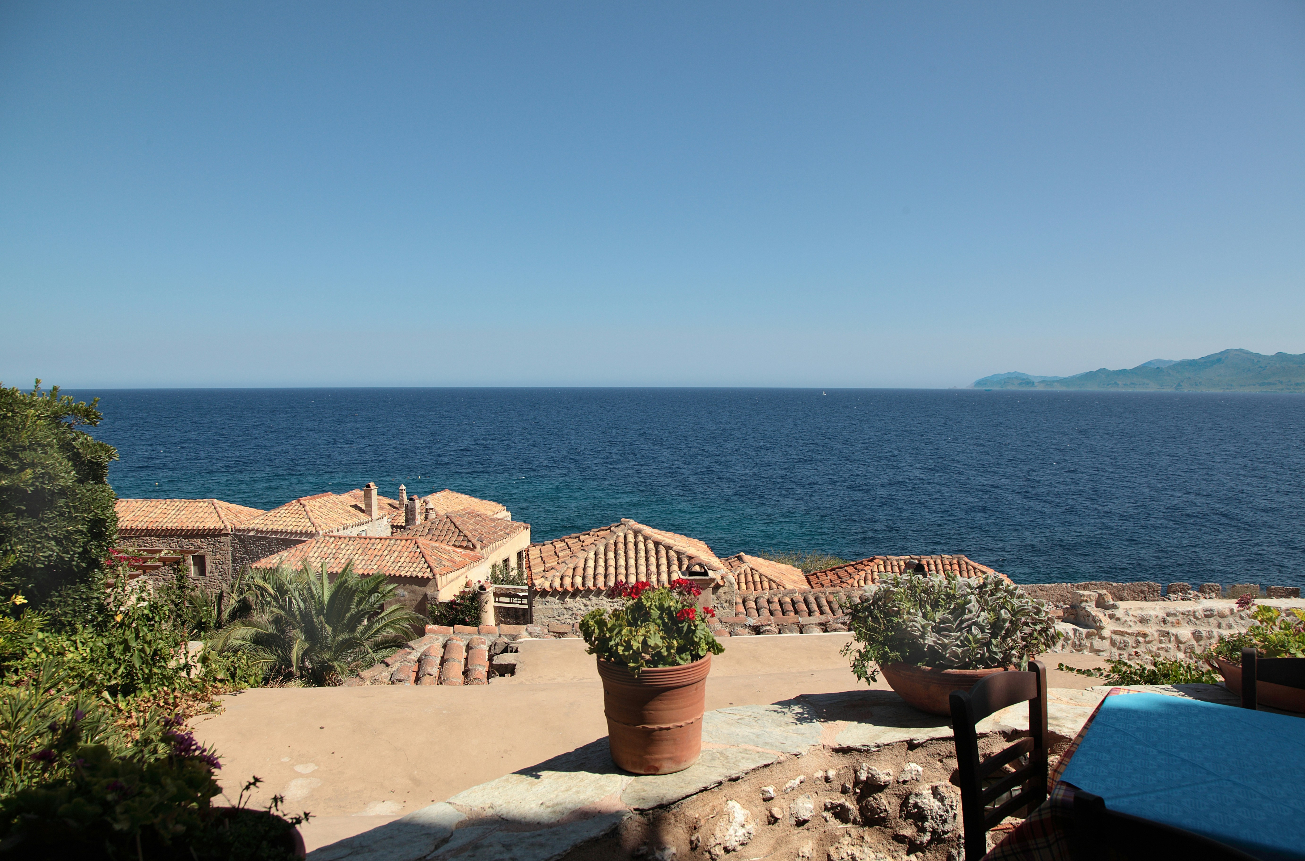 Terraced buildings overlook a calm blue ocean under clear skies.