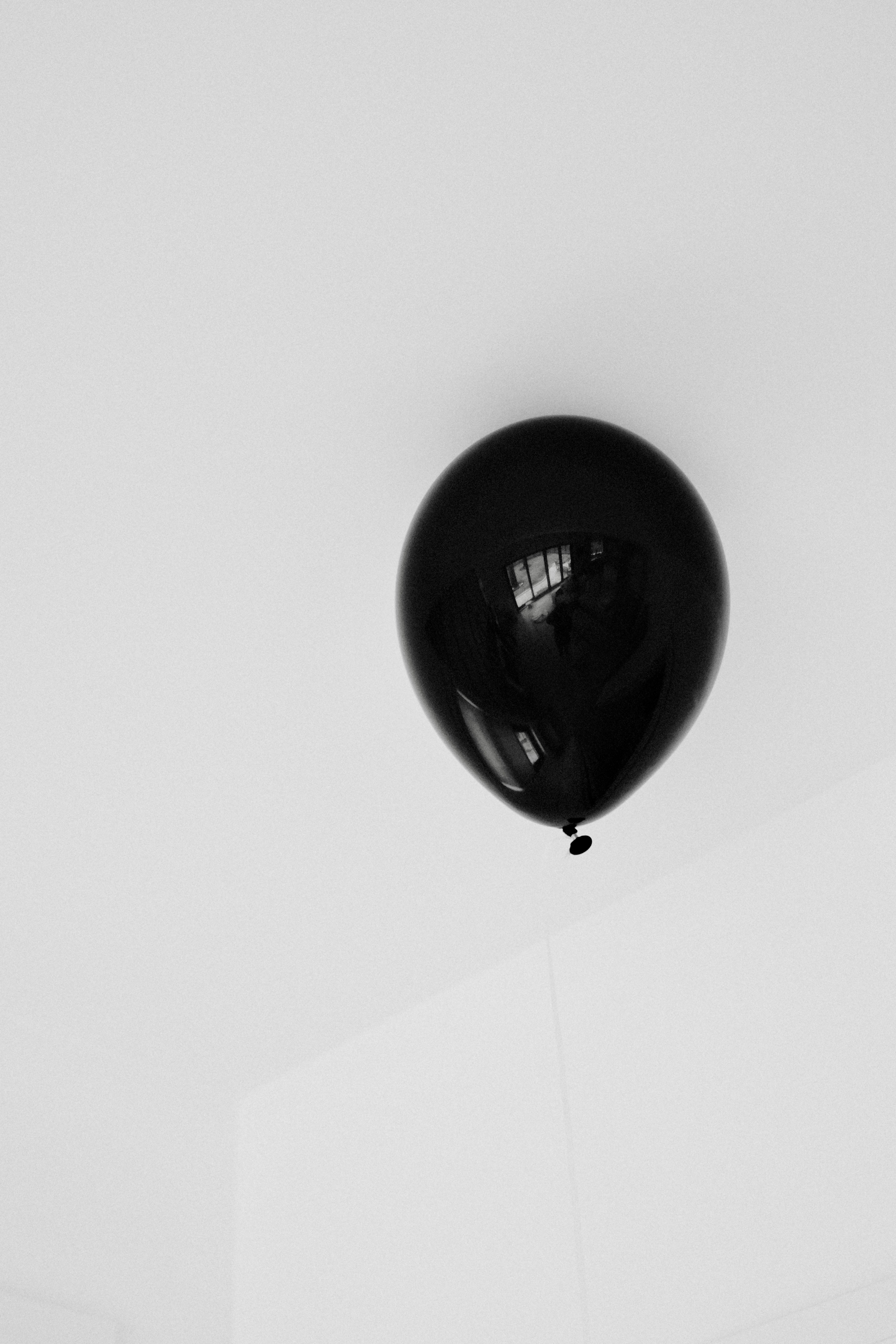 A single black balloon floats against a white wall.