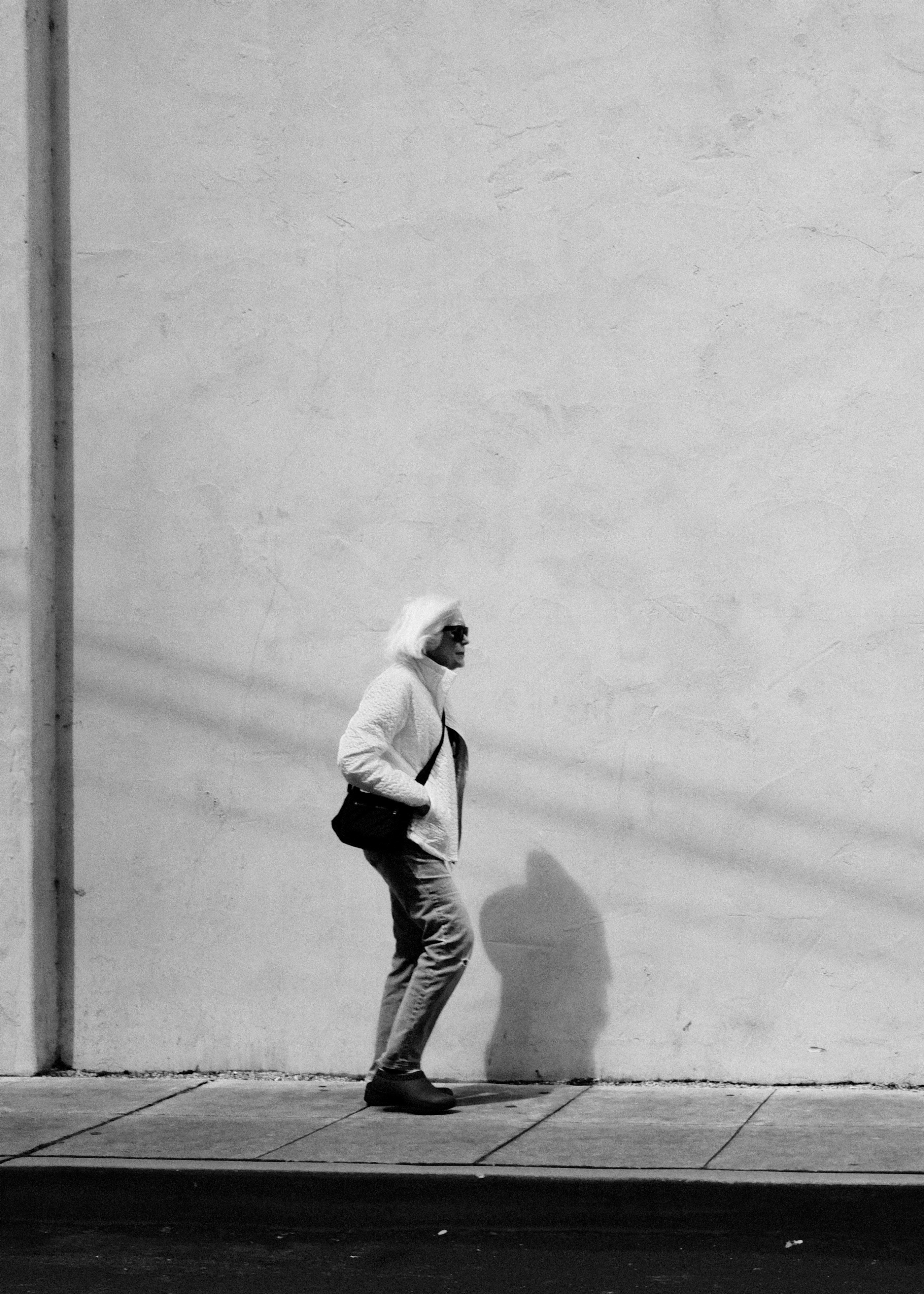 Elderly woman walks beside a textured wall