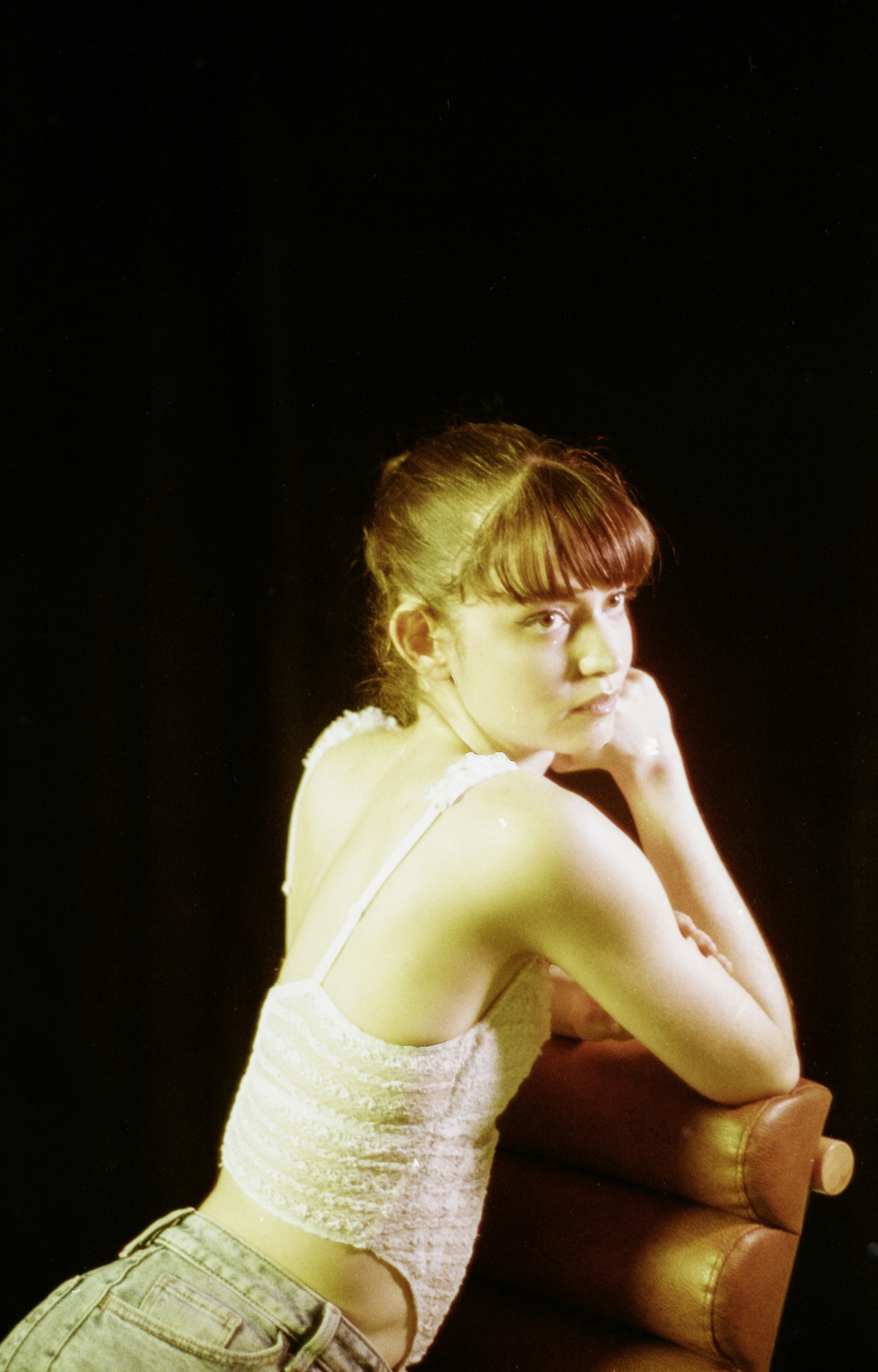 Young woman with bangs leans on chair armrest, looking away.