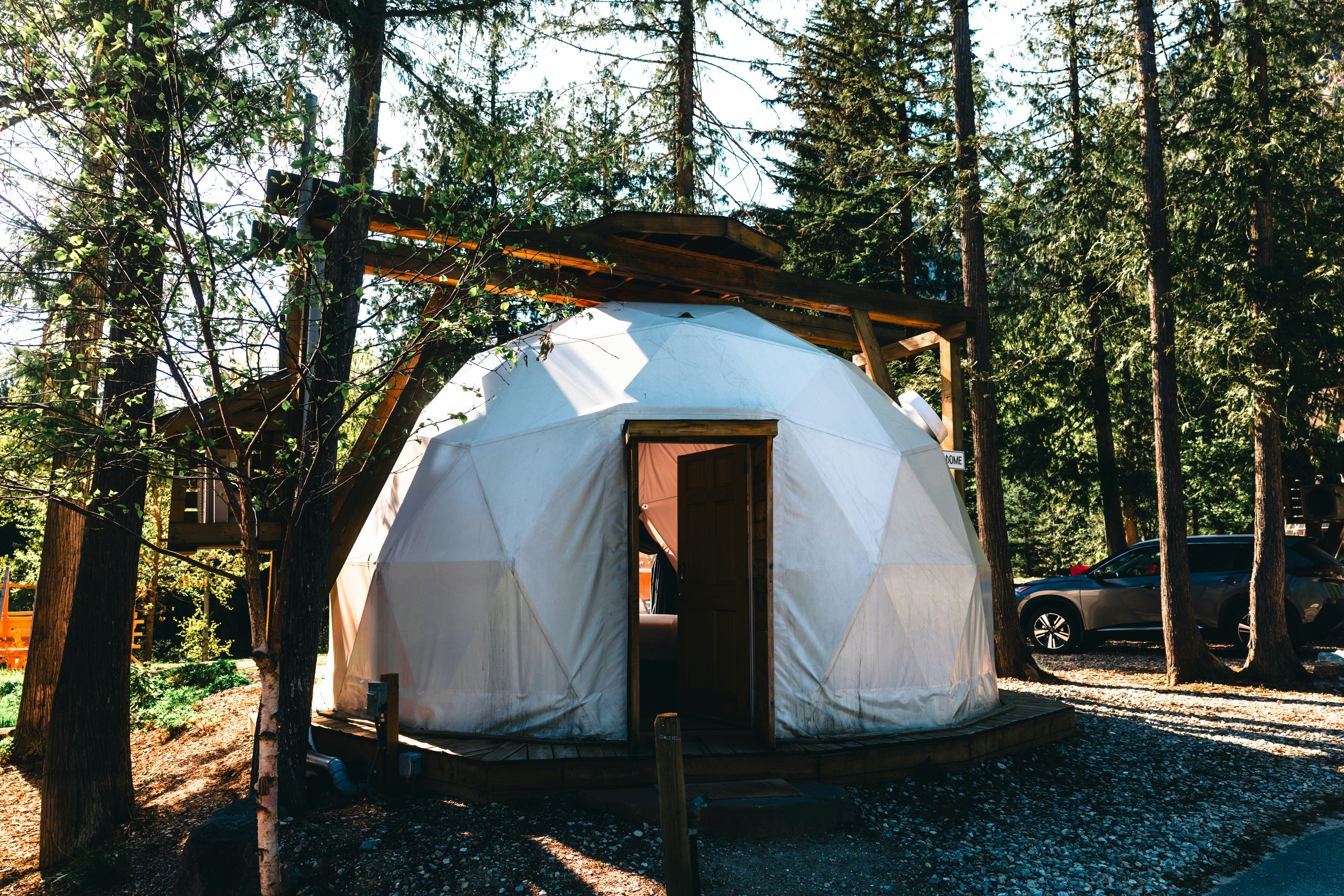 Una tenda a cupola geodetica bianca in un contesto forestale.