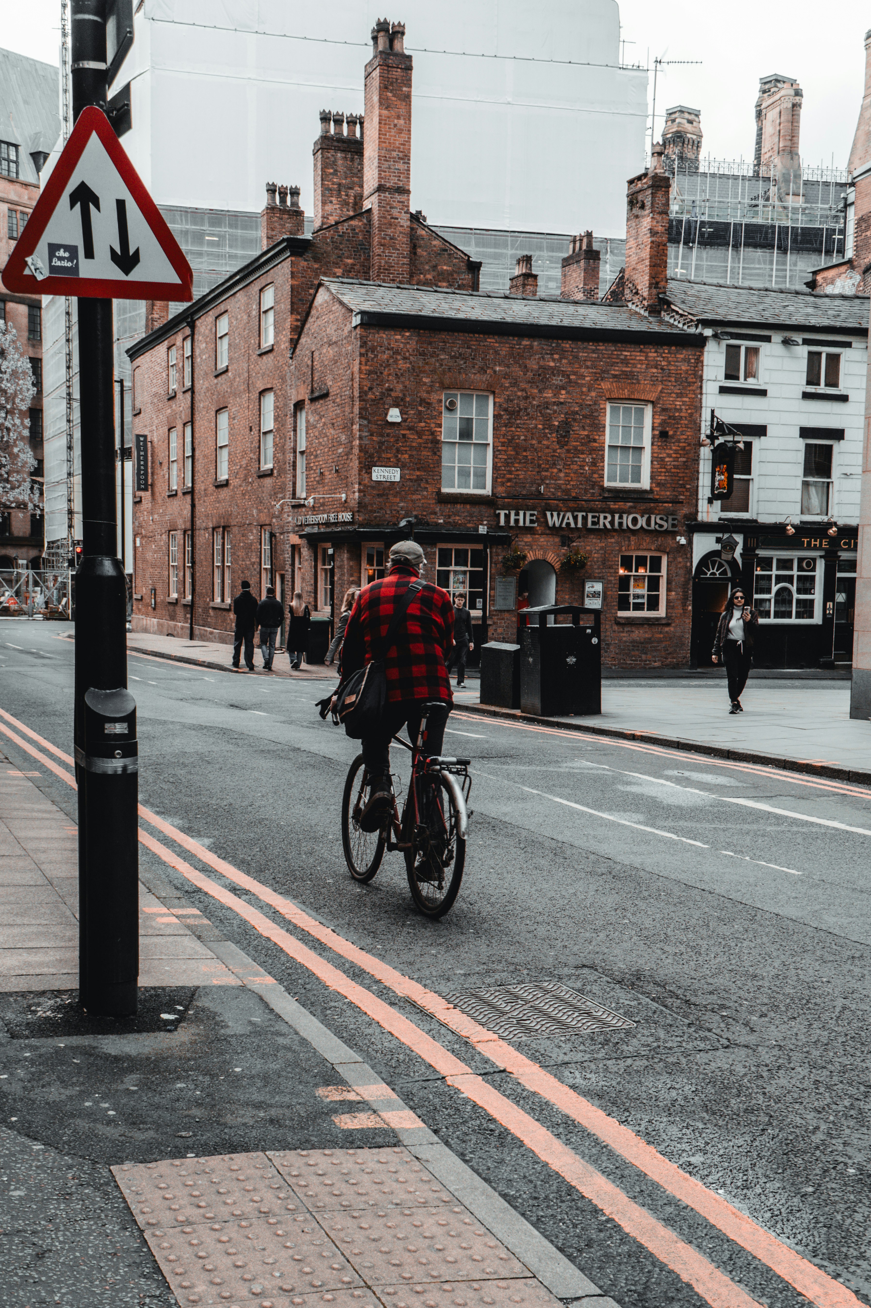 Man in red plaid shirt cycles down street.