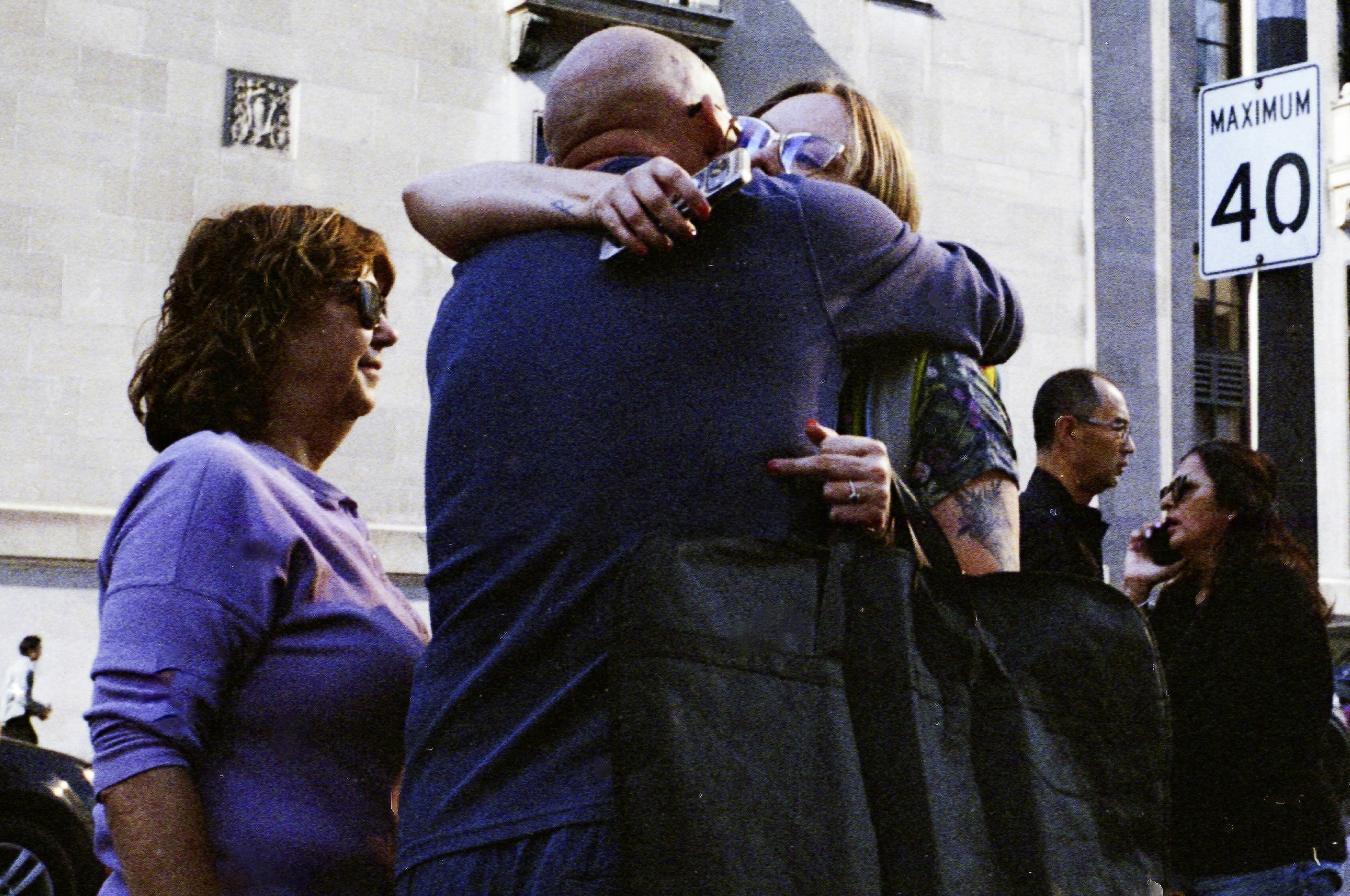 Two people hug while others watch in background.