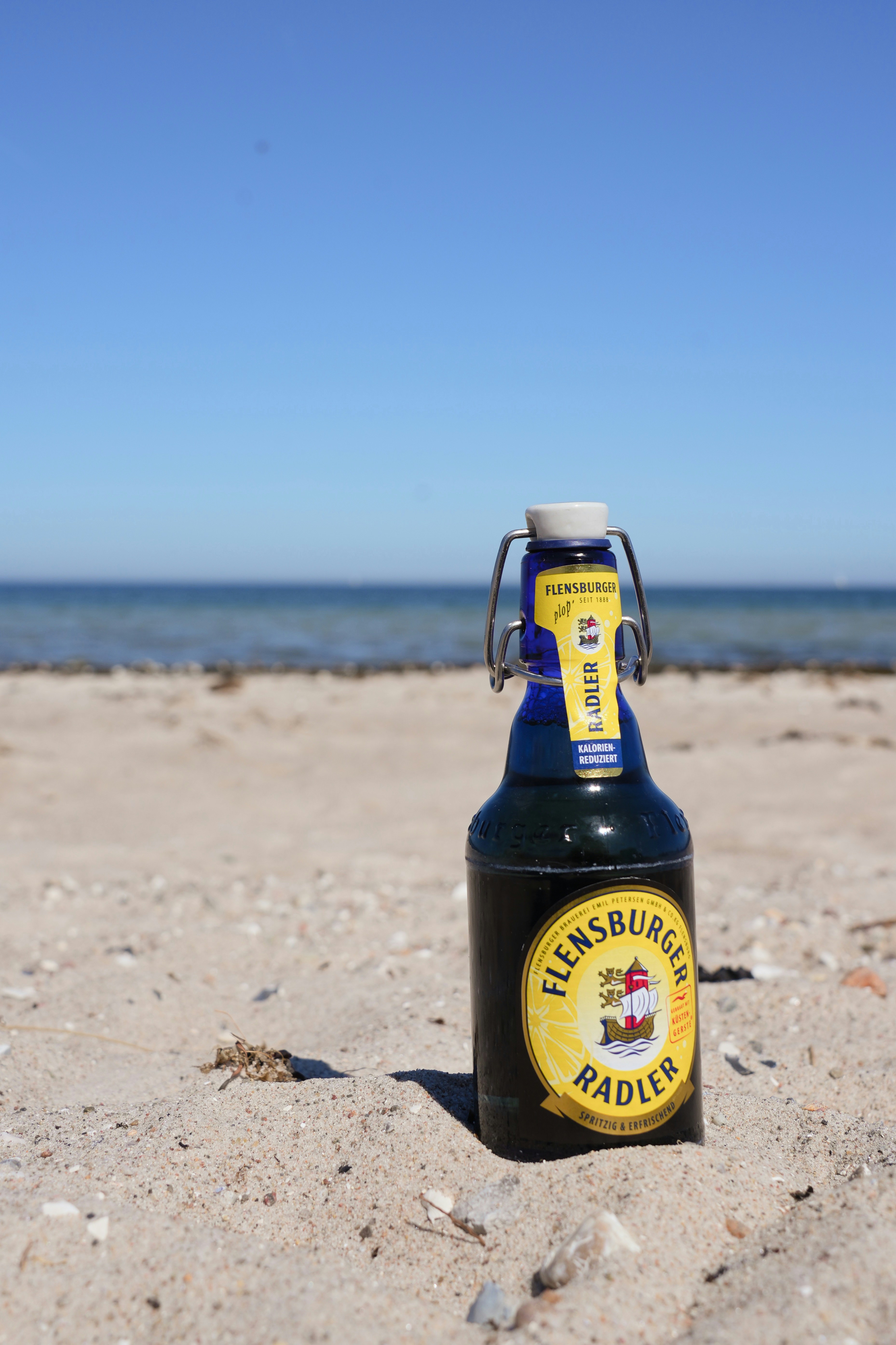 Une bouteille de flensburger radler sur une plage de sable.