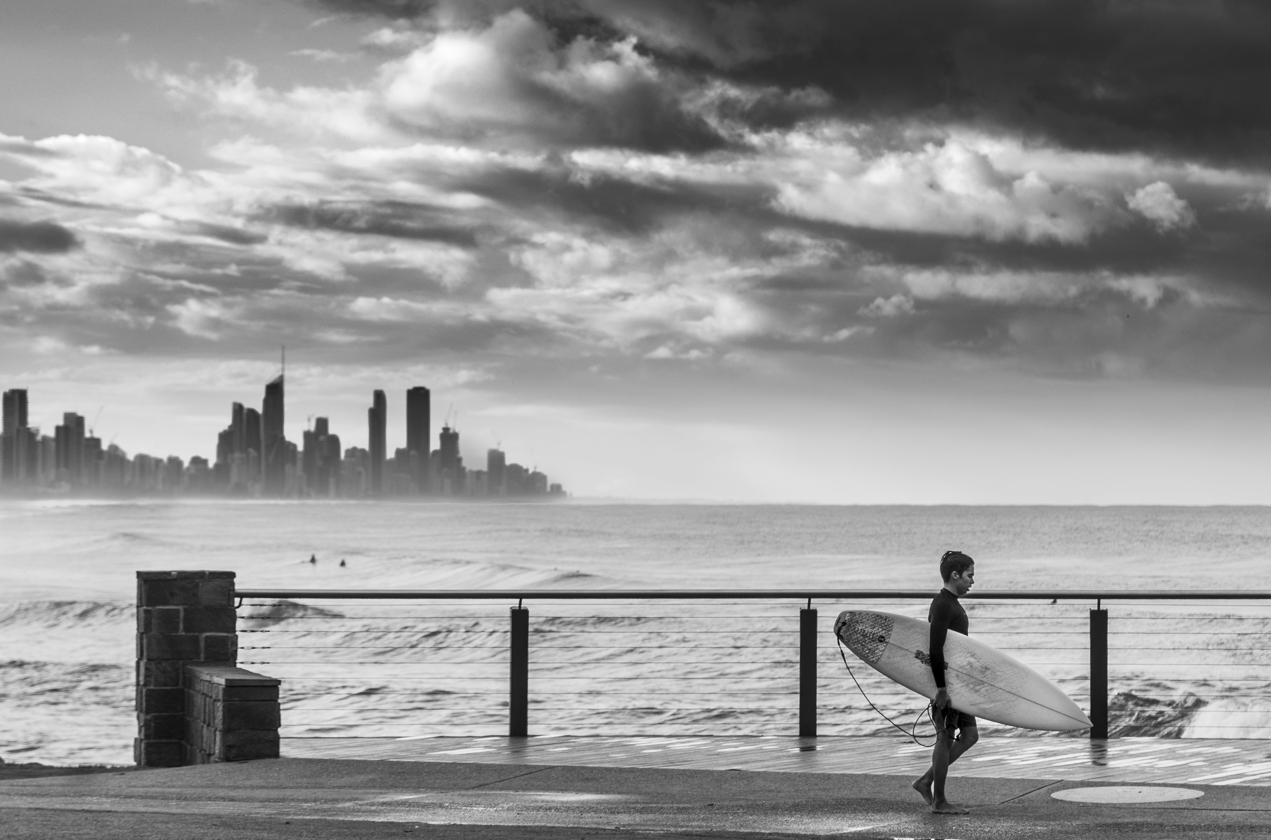 Un surfeur se promène le long de la plage avec la silhouette de la ville.